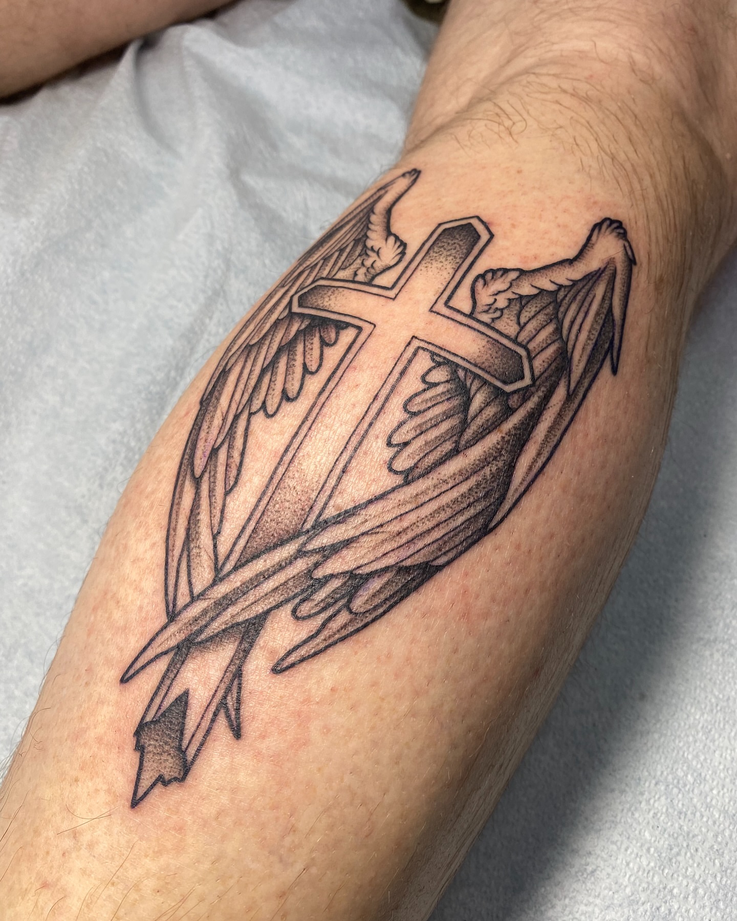 Cross with wings black and grey tattoo on the forearm by Ramsie Segura-Andrews
