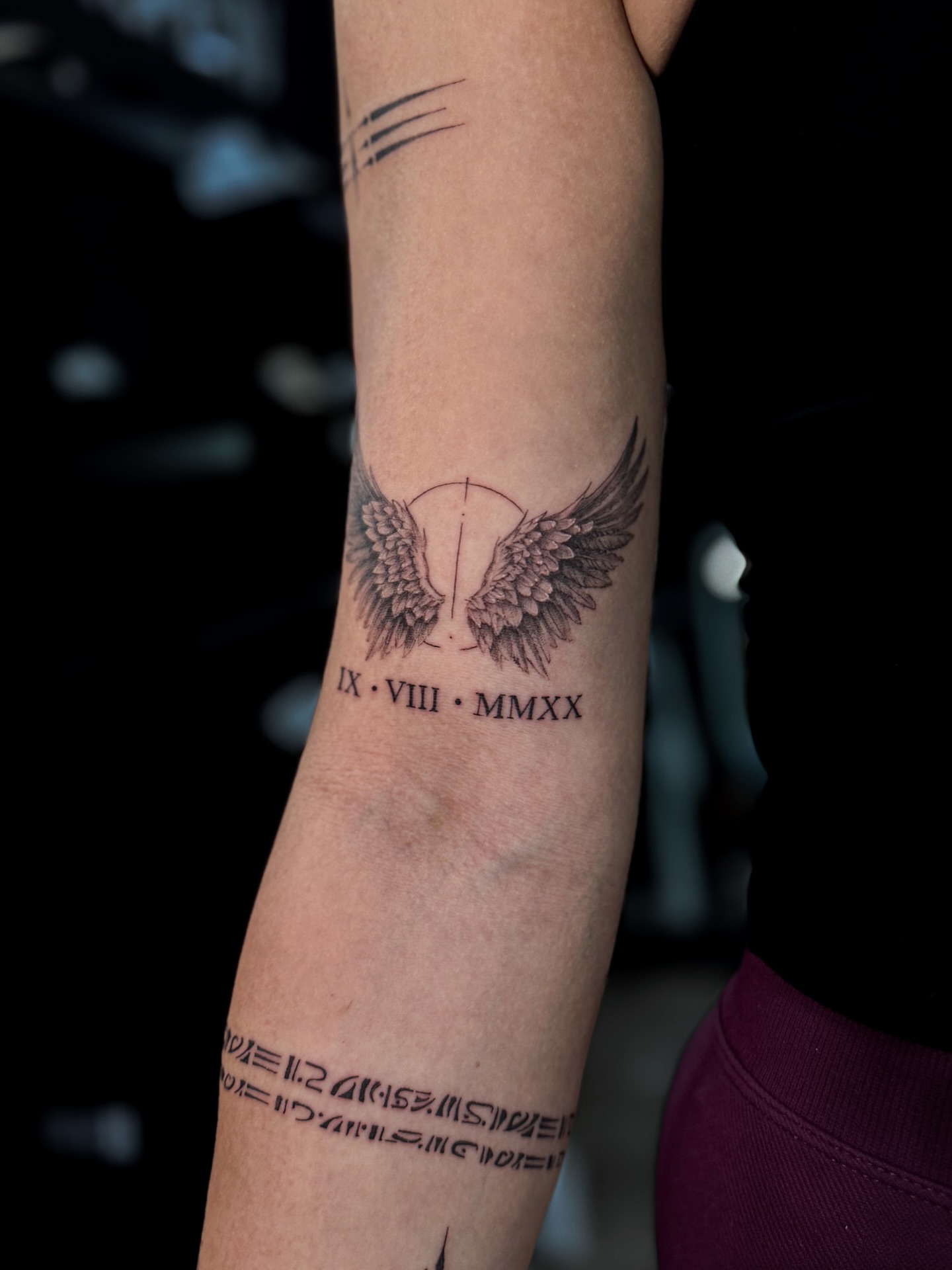 Wings and Roman numerals black and grey tattoo on the forearm by Nicolas Herrera