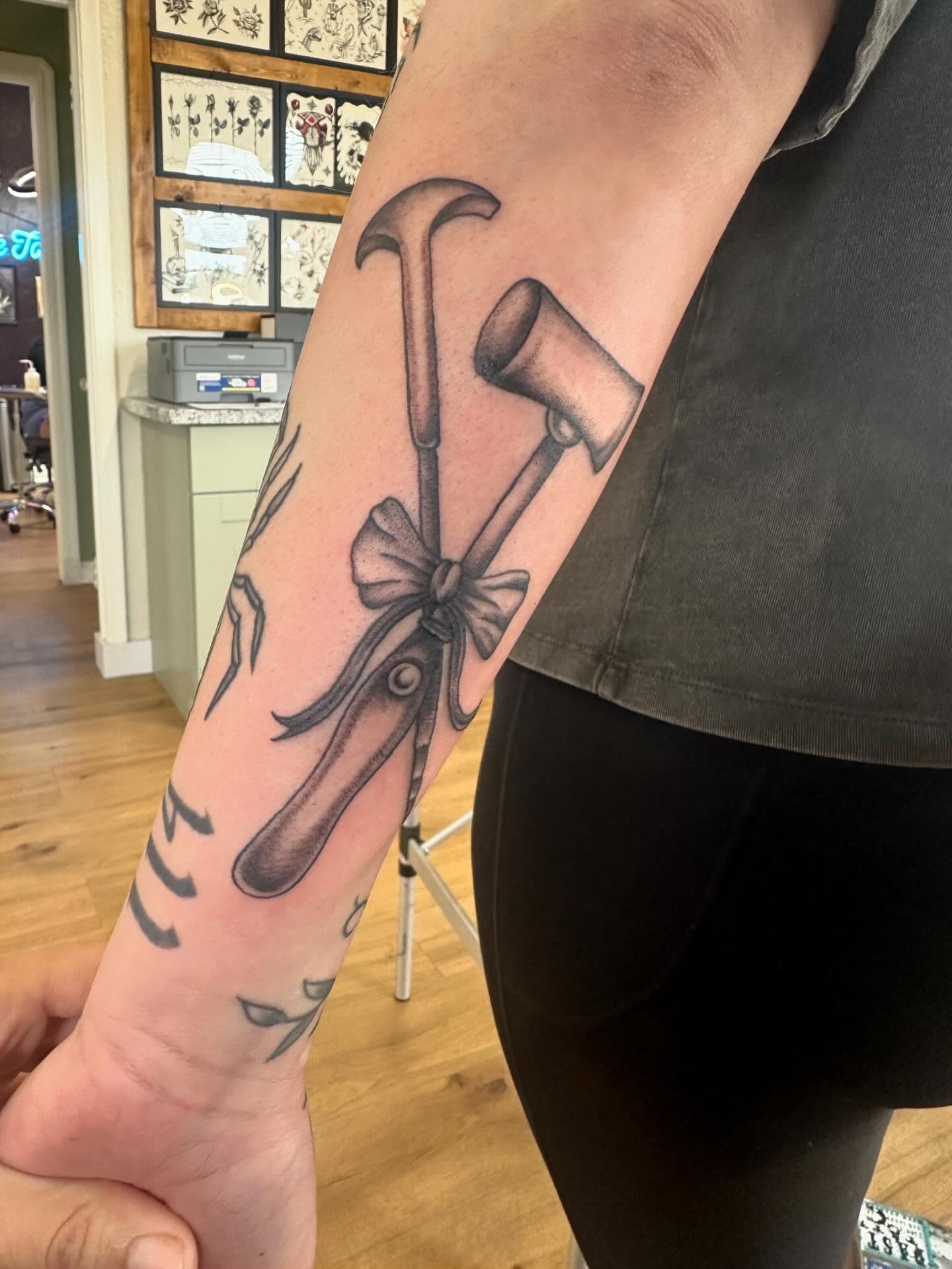 Hammer and axe black and grey tattoo on the forearm by Kaylee Woods