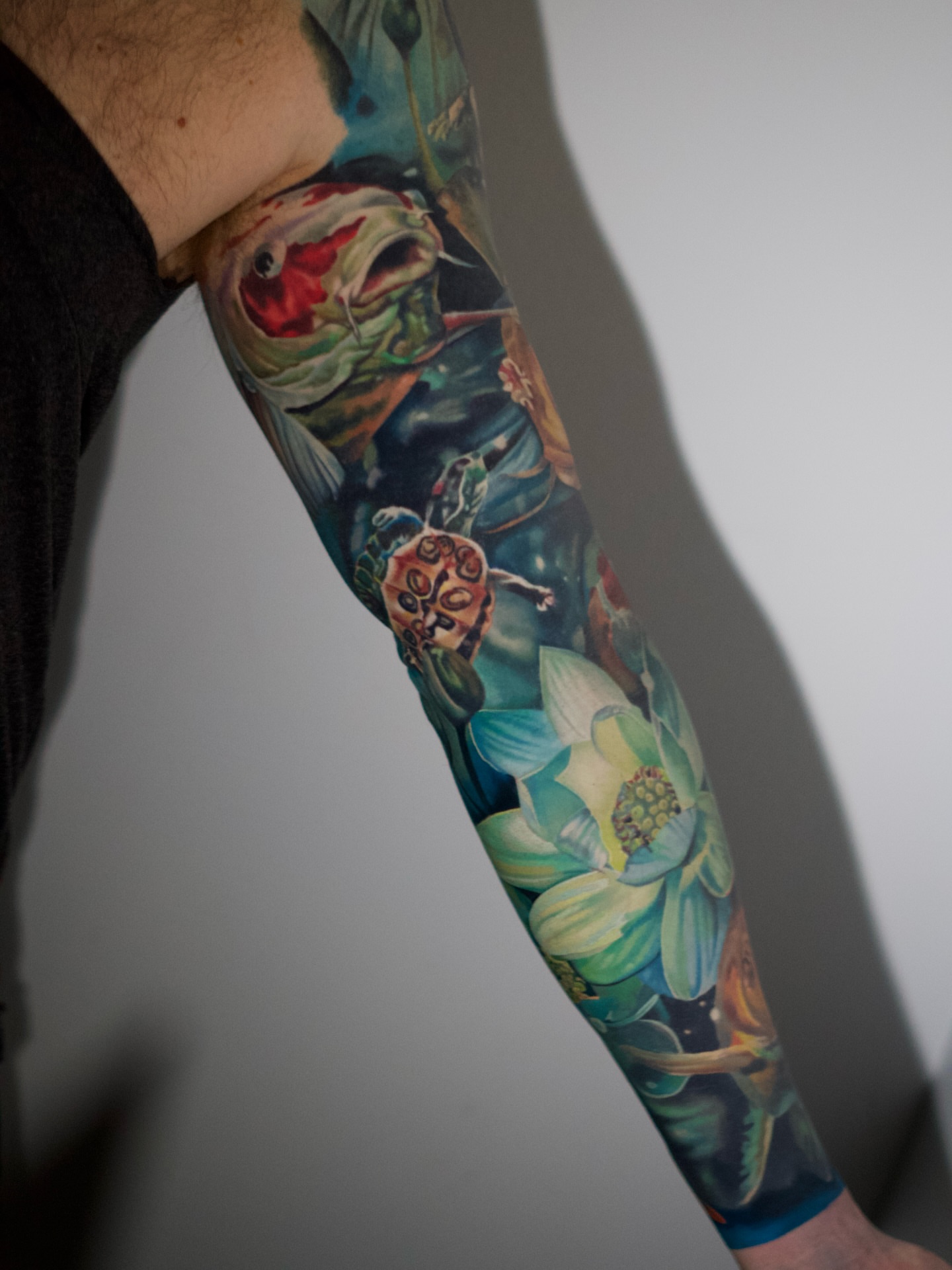 Fish and lotus realism tattoo on the forearm by Justin Shelpman