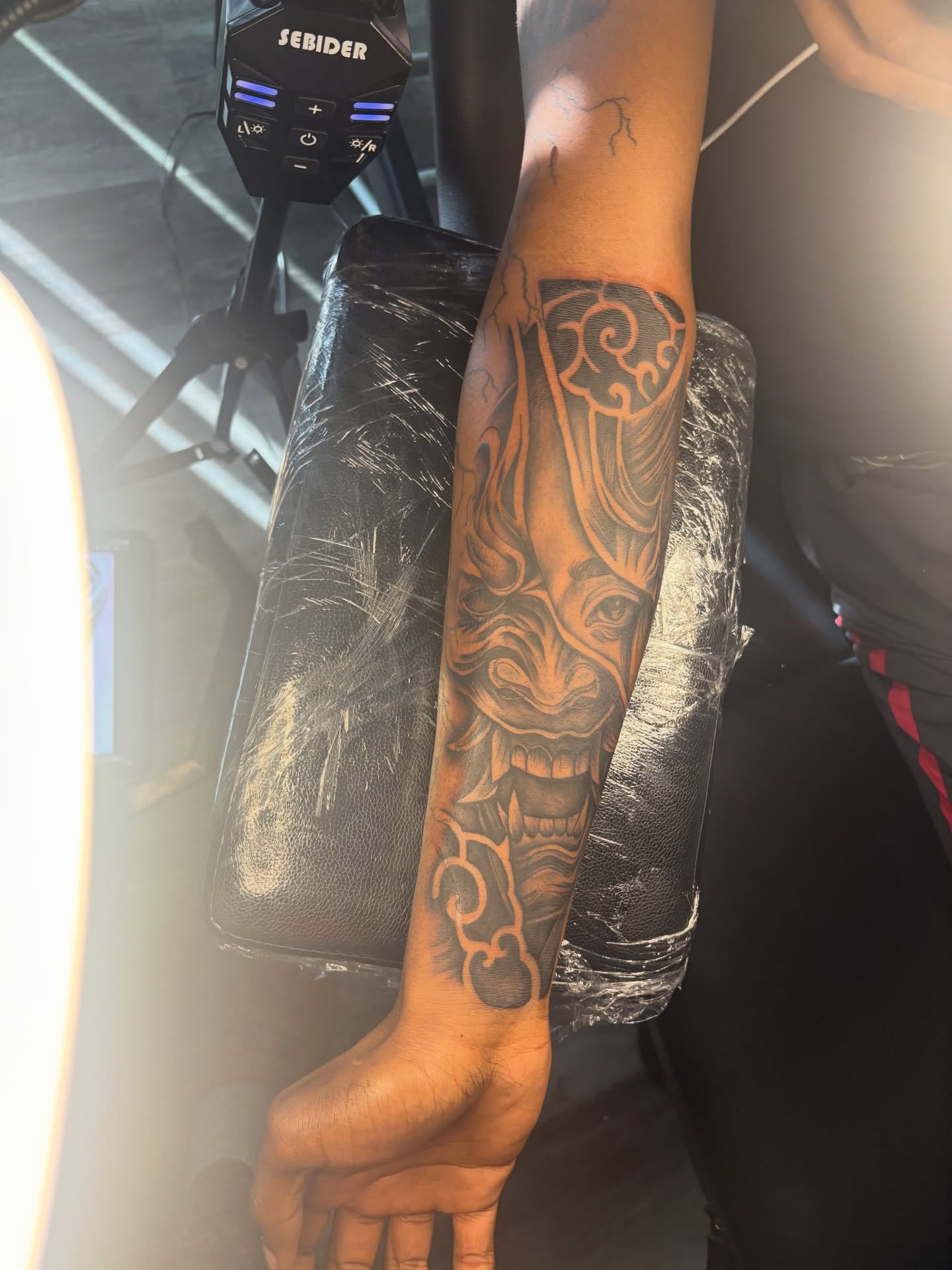 Mask black and grey tattoo on the forearm by Maleek Inkz