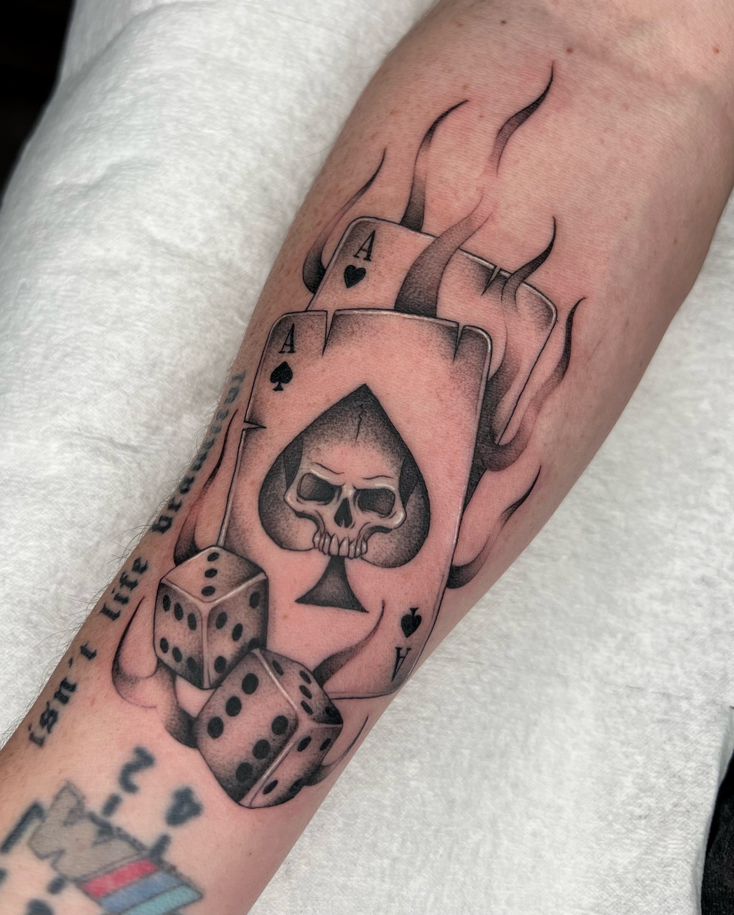 Playing card and skull black and grey tattoo on the forearm by 𝔐𝔦𝔠𝔥𝔢𝔩𝔩𝔢 ℭ𝔥𝔞𝔪𝔢𝔯𝔩𝔦𝔨