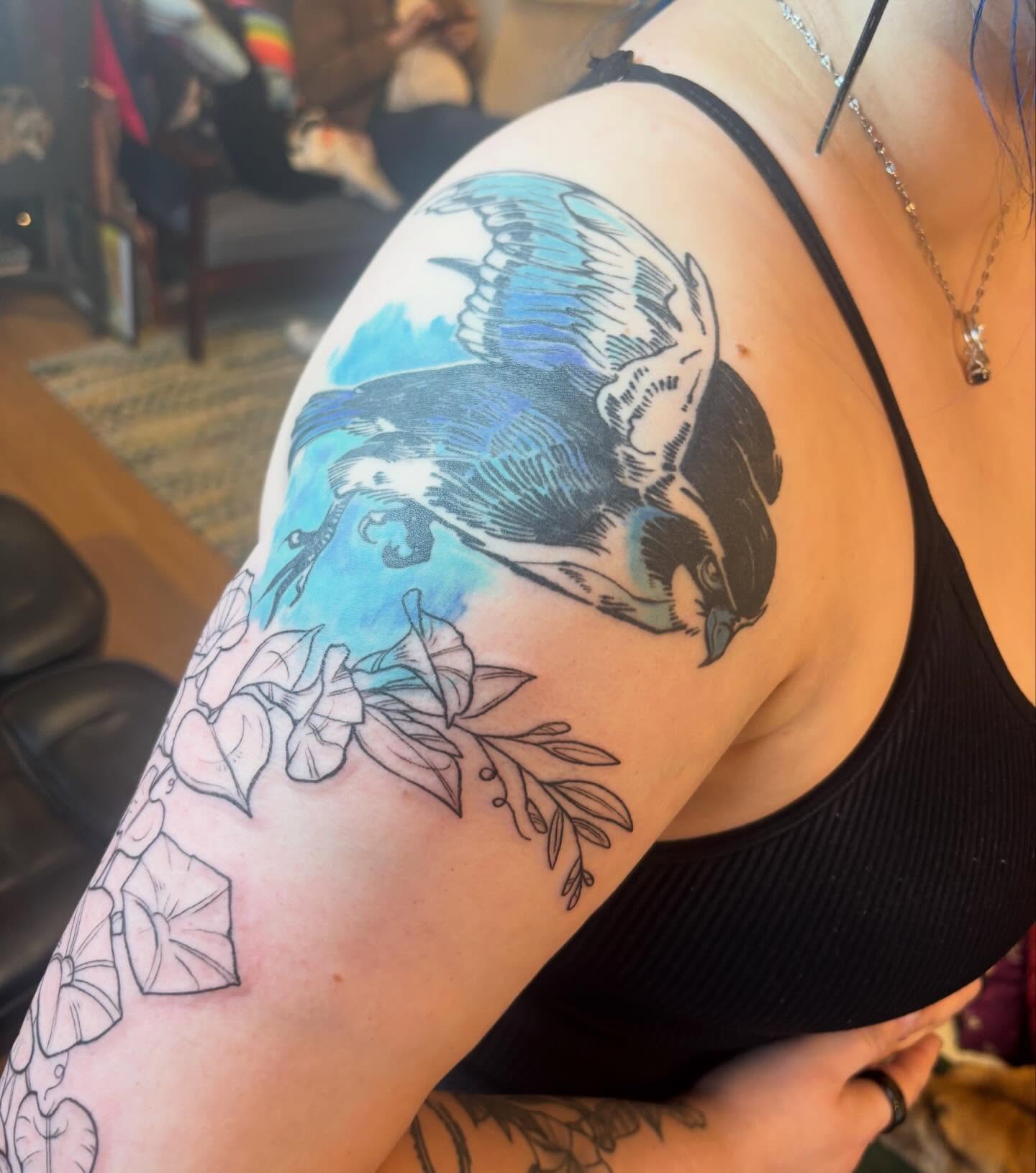 Bird and flowers watercolor tattoo on the upper arm by Zoe Brookes