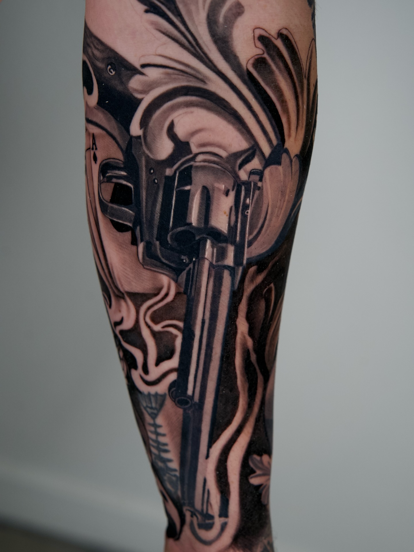 Gun and floral realism tattoo on the forearm by Travis