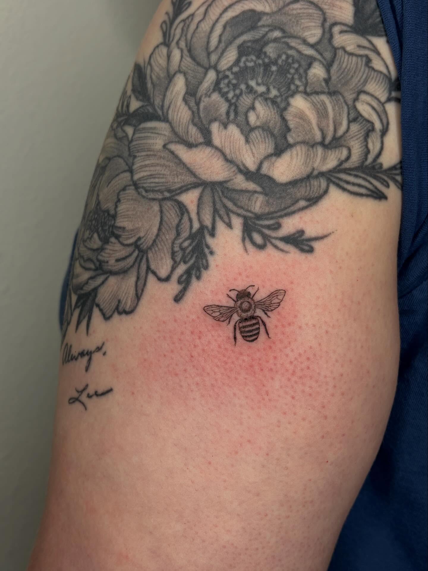 Bee and floral black and grey tattoo on the upper arm by alyssa doing tattoos