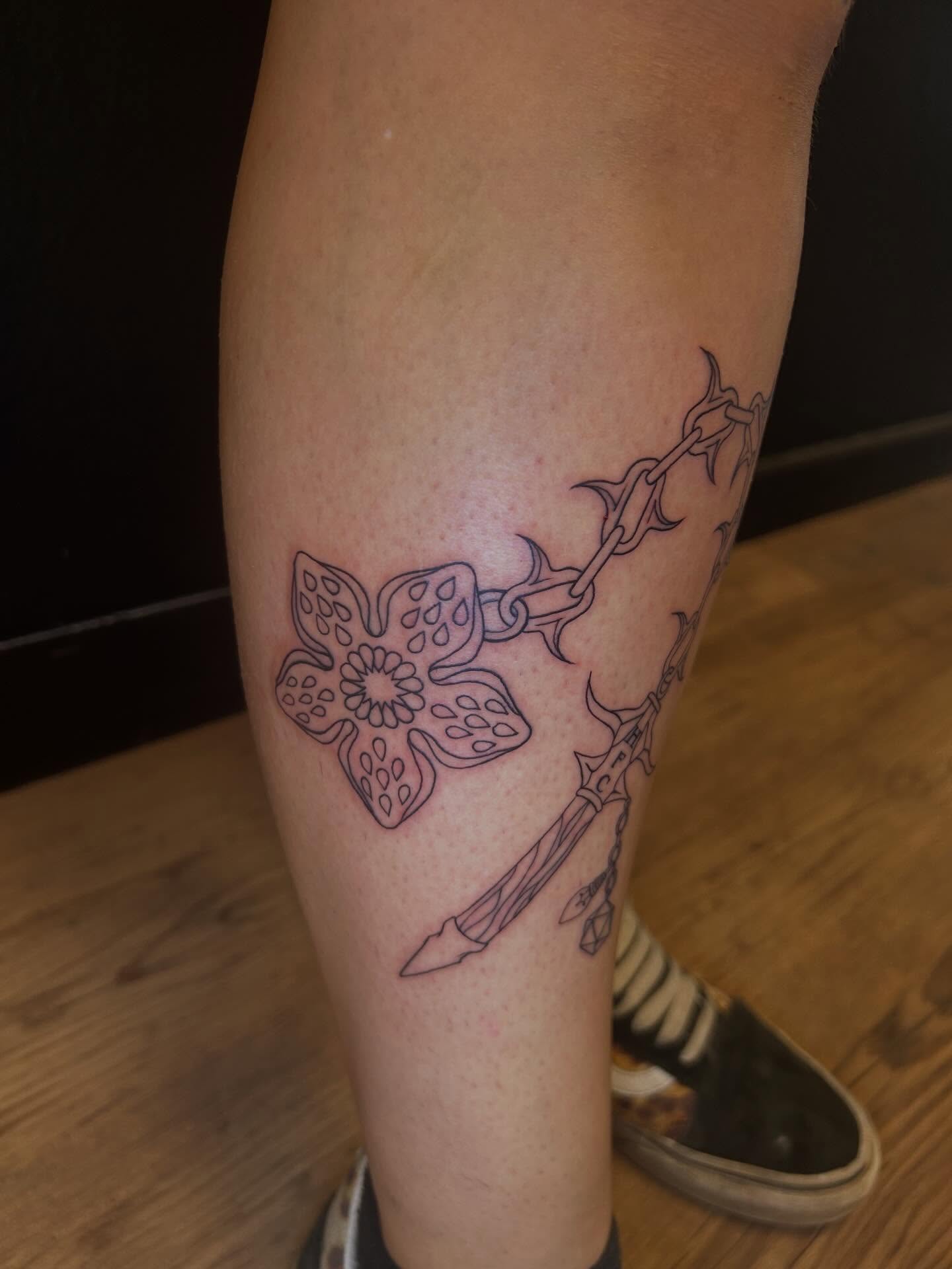 Sword and flower black and grey tattoo on the leg by Ashley Lambert