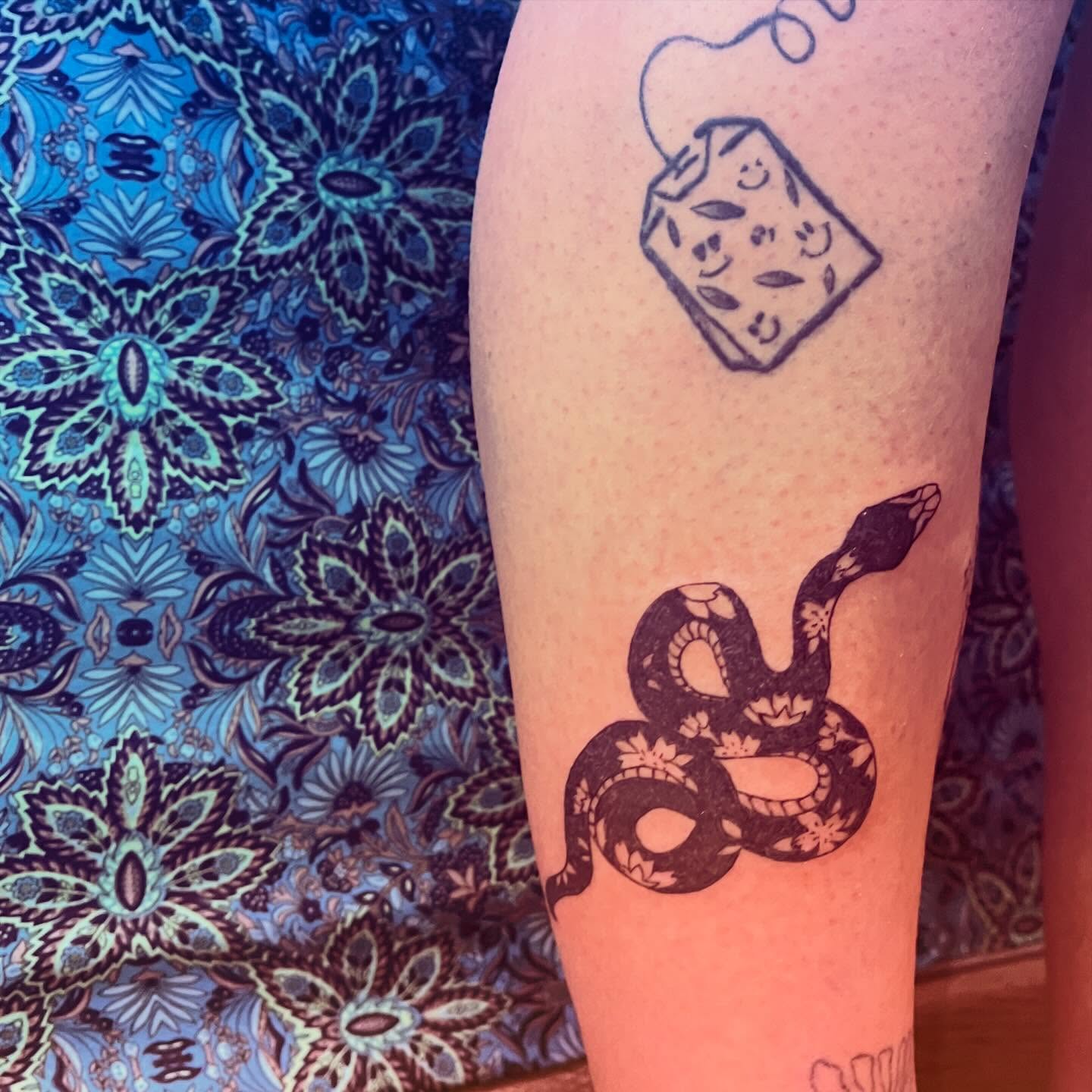 Snake and tea bag black and grey tattoo on the forearm by La Main Bleue