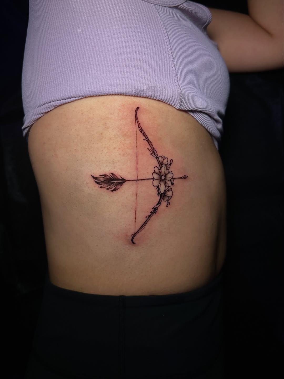 Bow and arrow with flowers fine line tattoo on the ribs by Dennis Alejandro