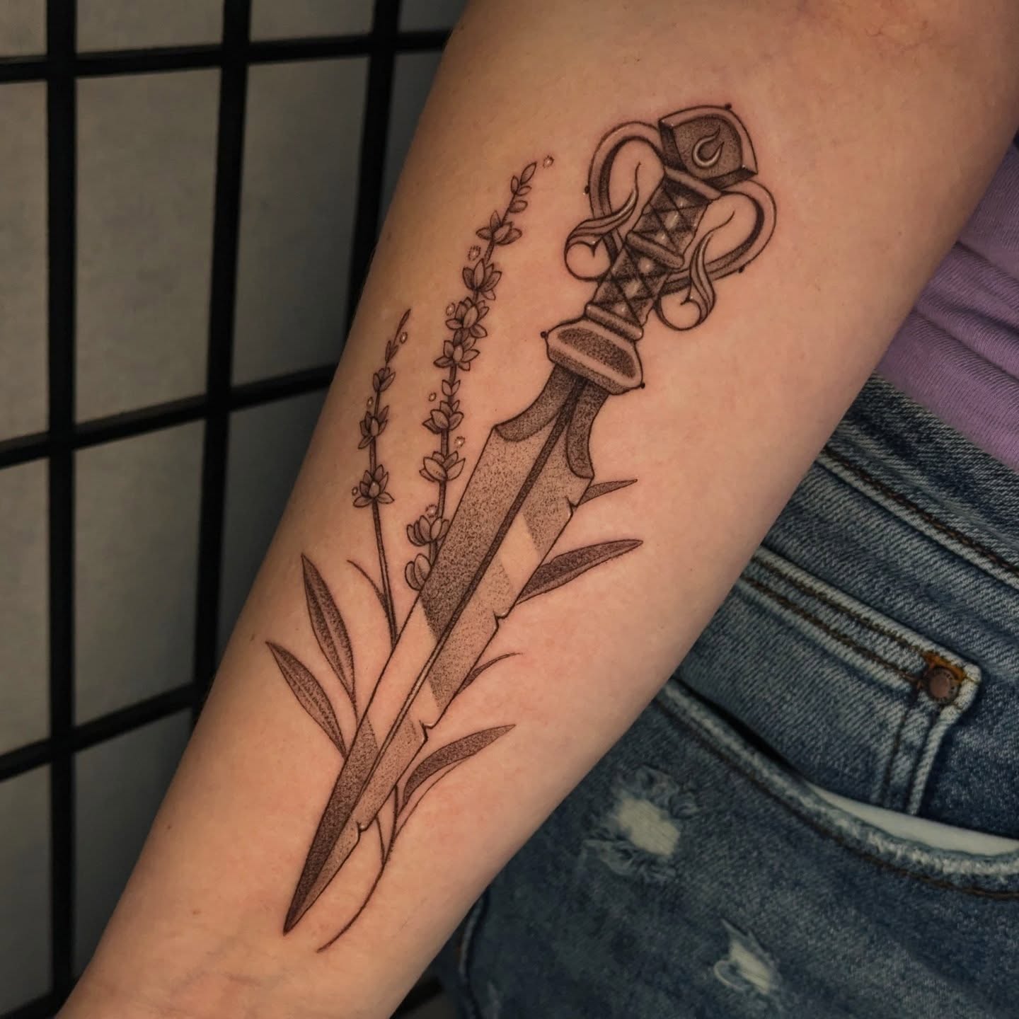 Sword and flowers black and grey tattoo on the forearm by Jasmine Dillon