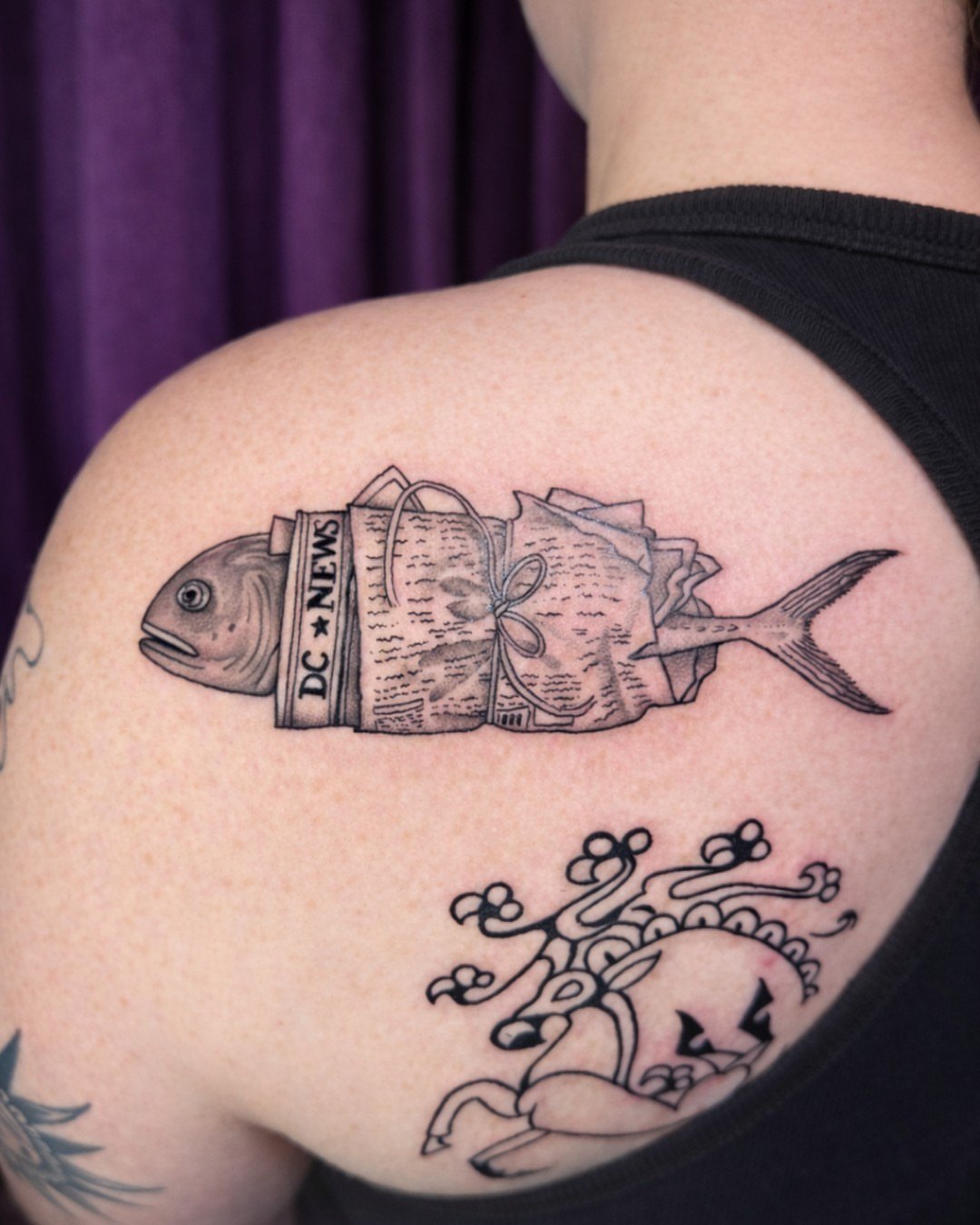 Fish with newspaper black and grey tattoo on the shoulder by Tattoos & Tea DC, Arlington, Virginia