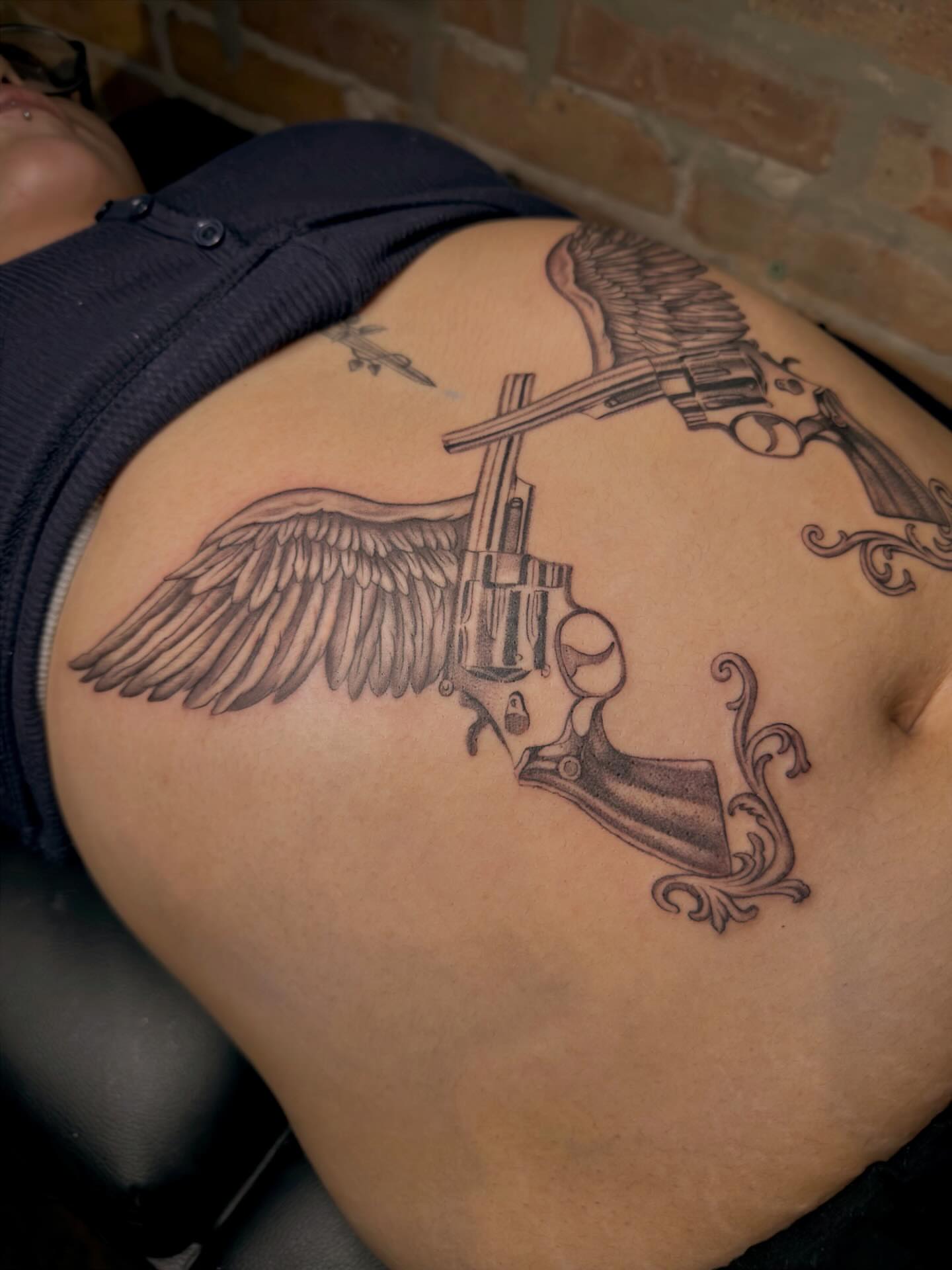 Winged revolver black and grey tattoo on the thigh by Nayoung, San Francisco, California