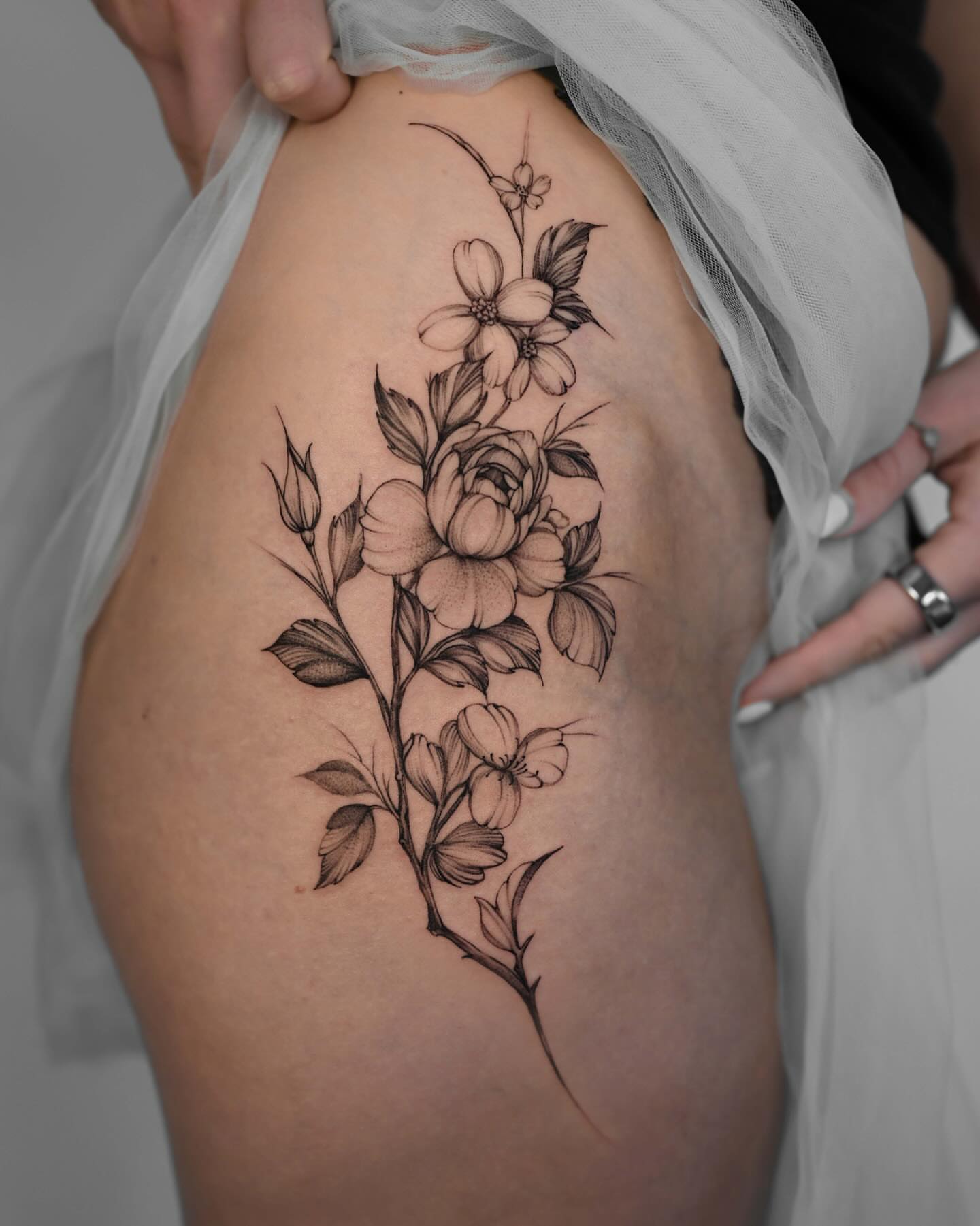 Floral bouquet black and grey tattoo on the thigh by Anastasiia