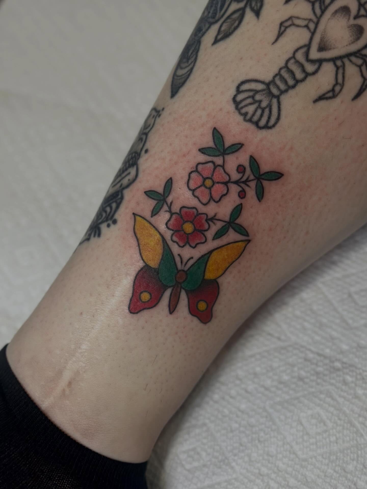Butterfly and flowers American traditional tattoo on the forearm by Kat Fishbein