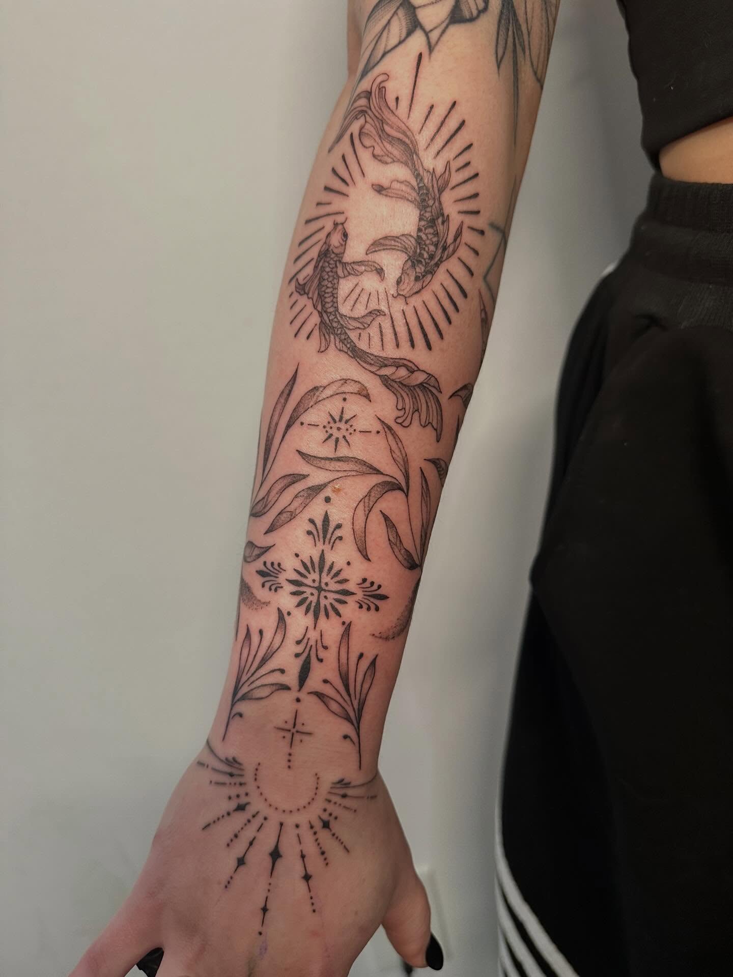 Fish and floral black and grey tattoo on the forearm by Miesha Busker