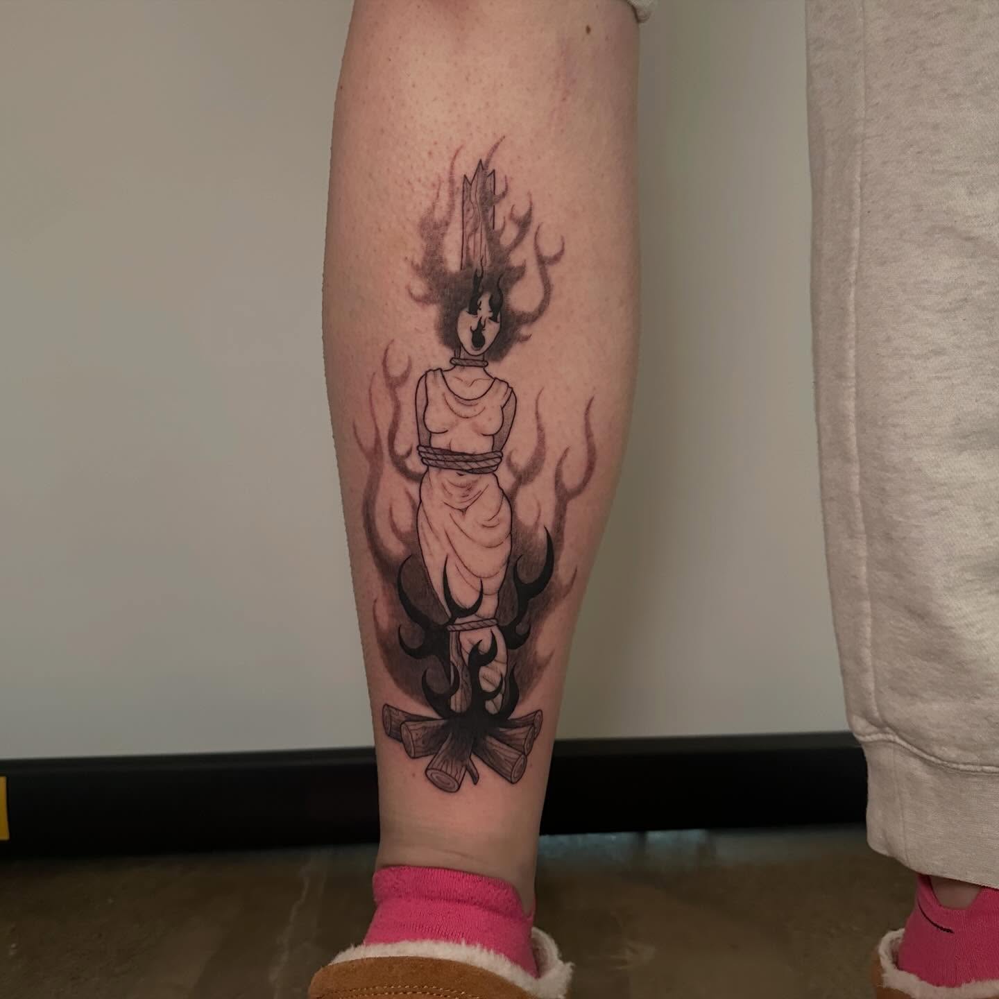 Flame-wrapped figure black and grey tattoo on the calf by Nia Malone (Knee-Uh)