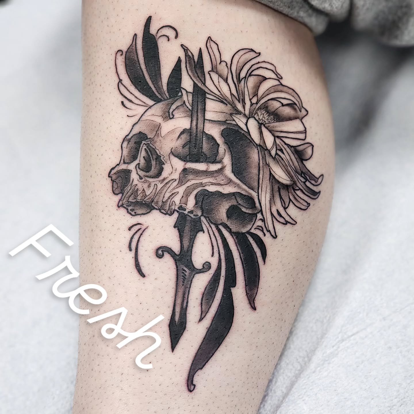 Skull with flowers black and grey tattoo on the thigh by Robert Glover
