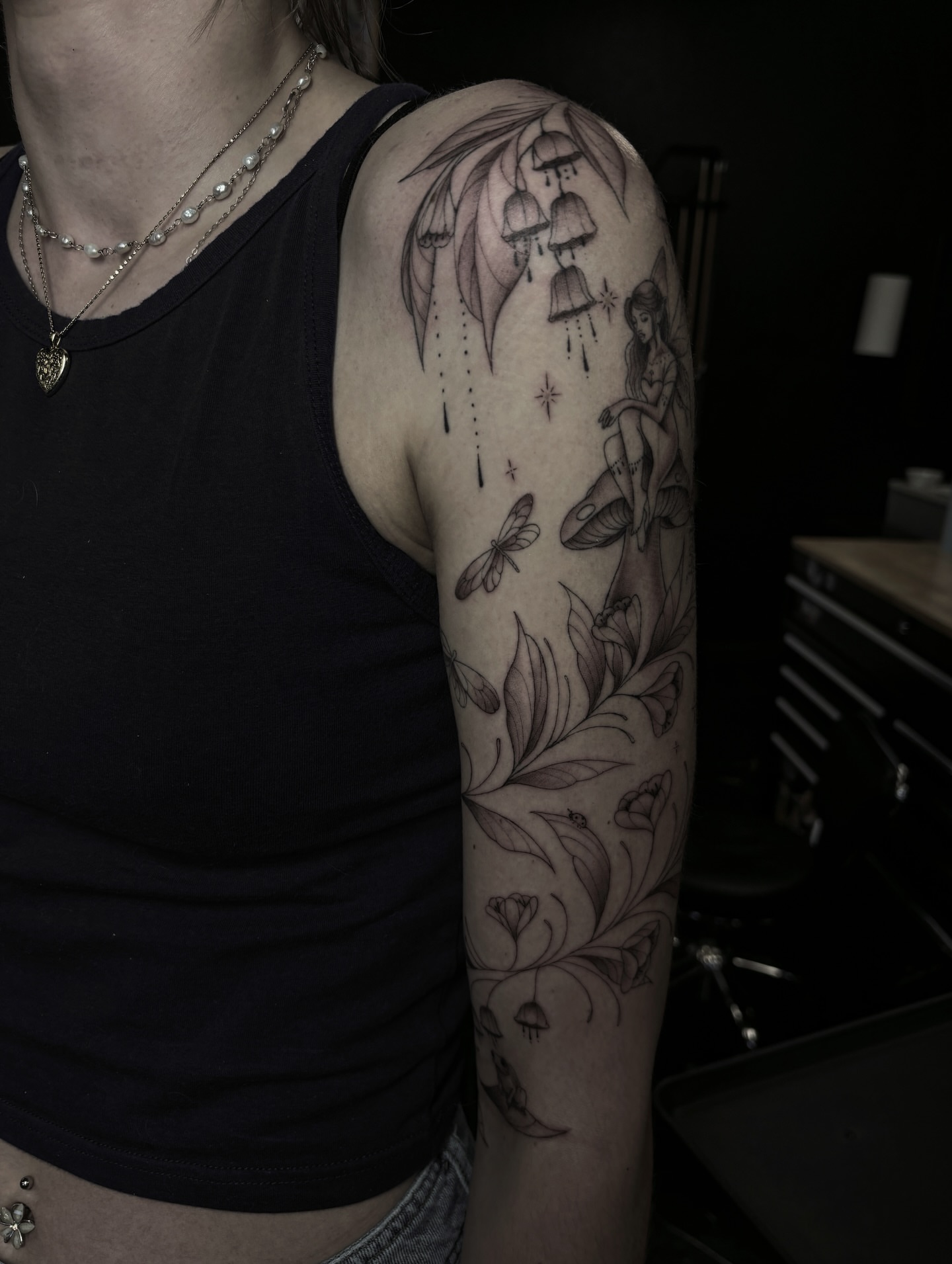 Bell and fairy black and grey tattoo on the upper arm by Fine Line Tattoo Artist