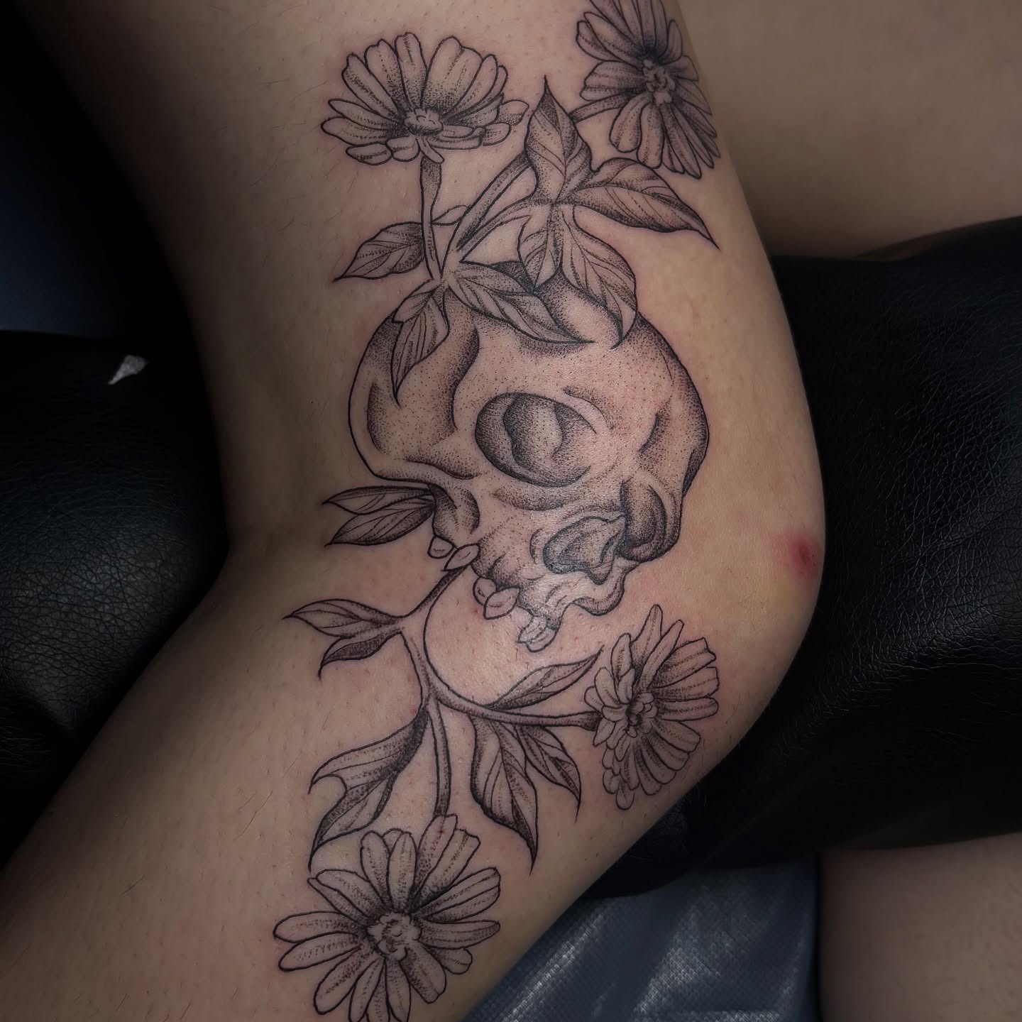 Skull and flowers dotwork tattoo on the thigh by Sydney Gallucci