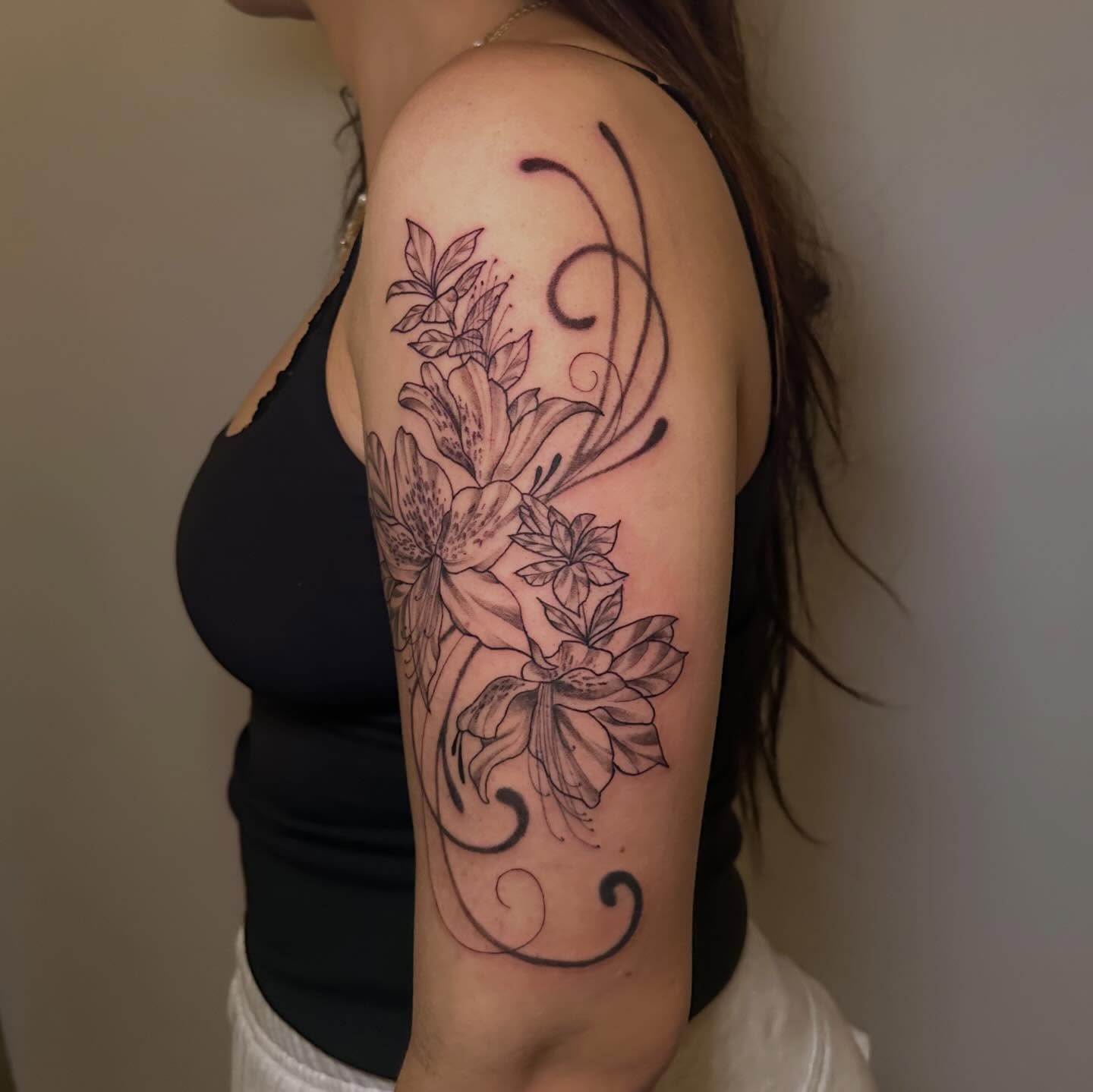 Lilies and swirls black and grey tattoo on the upper arm by Nia Malone (Knee-Uh)