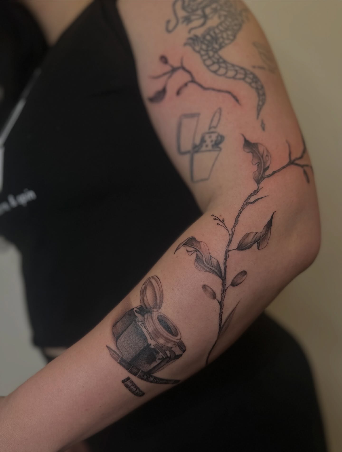 Camera and plant black and grey tattoo on the forearm by Macy Rae