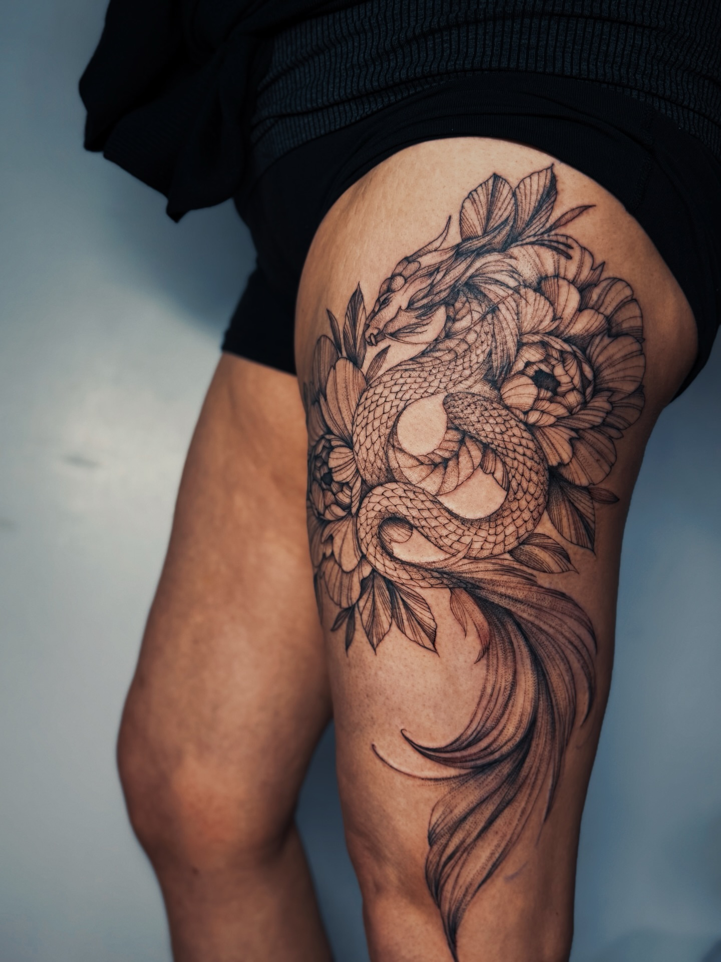 Dragon and flowers realism tattoo on the thigh by Olha Tytarenko