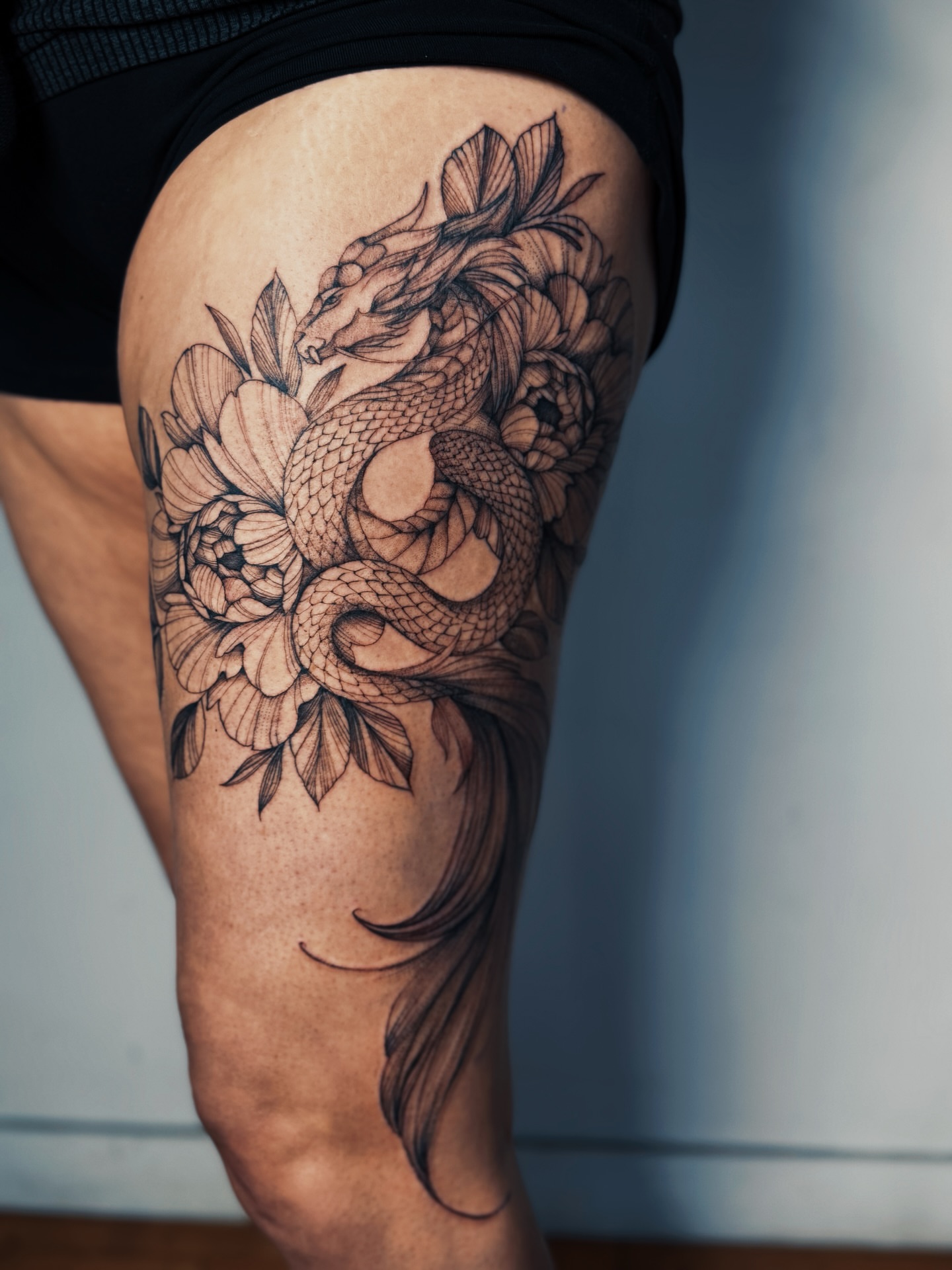 Dragon and flowers realism tattoo on the thigh by Olha Tytarenko