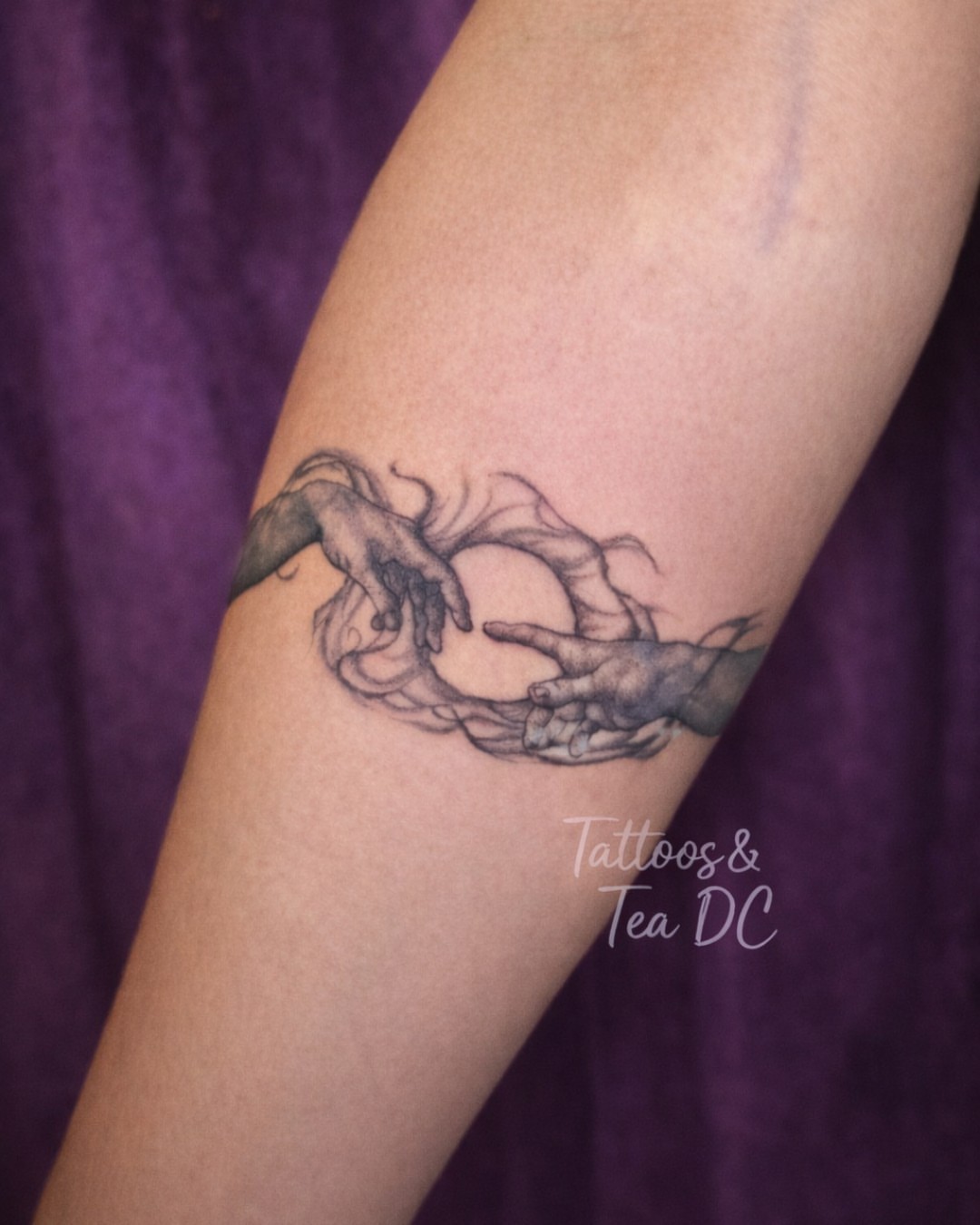 Two hands reaching towards a sphere black and grey tattoo on the forearm by Tattoos & Tea DC, Arlington, Virginia