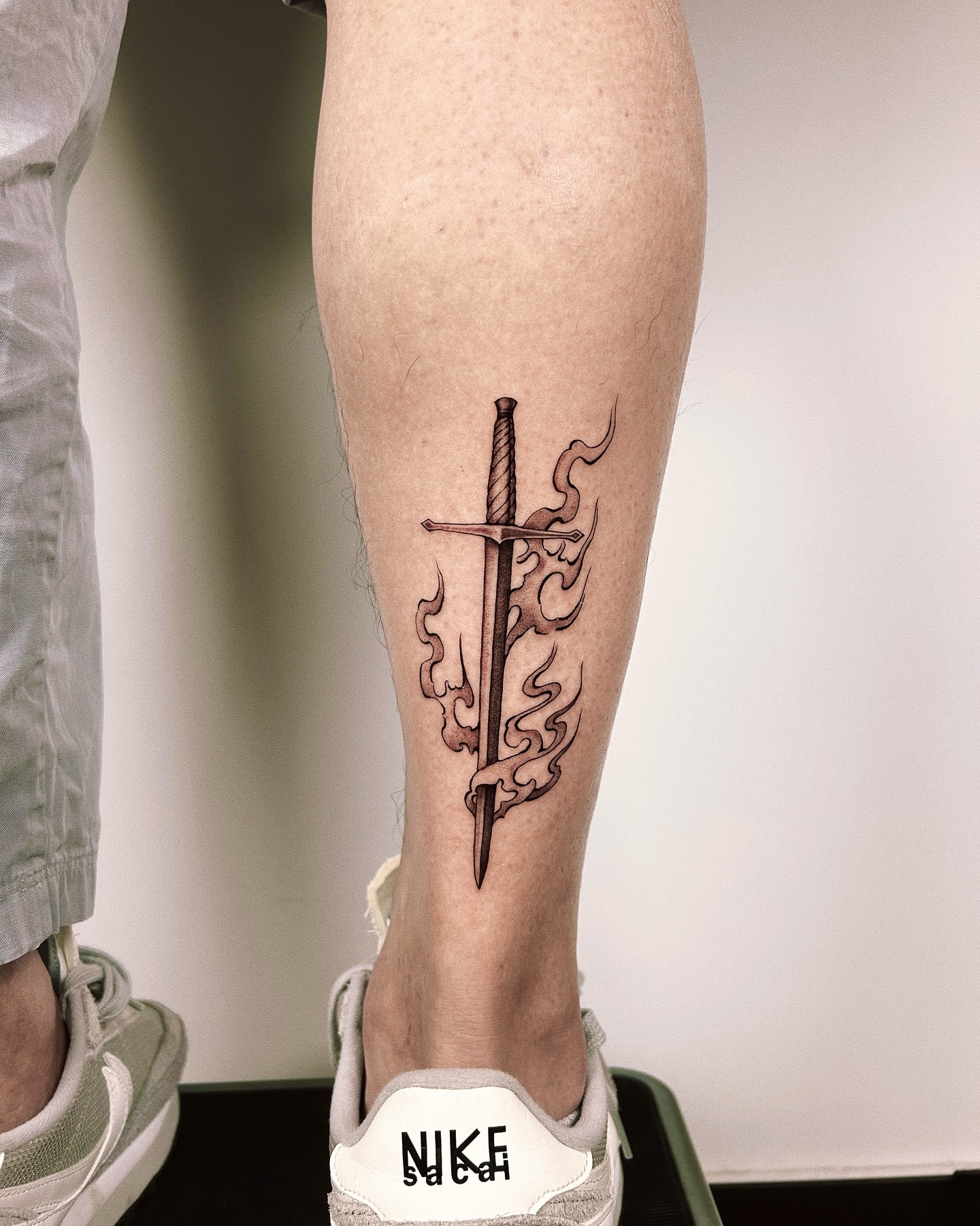 Sword with flames black and grey tattoo on the calf by Montana Chambers