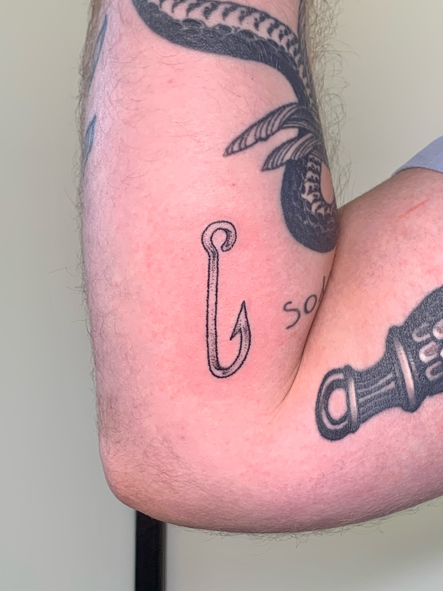 Fishing hook black and grey tattoo on the forearm by Lex Lloyd