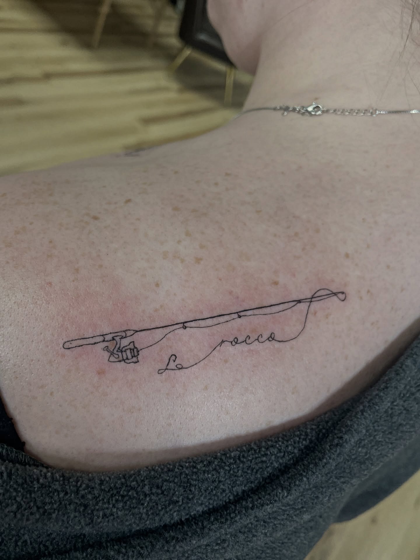Fishing rod fine line tattoo on the upper arm by Francesca Siwa