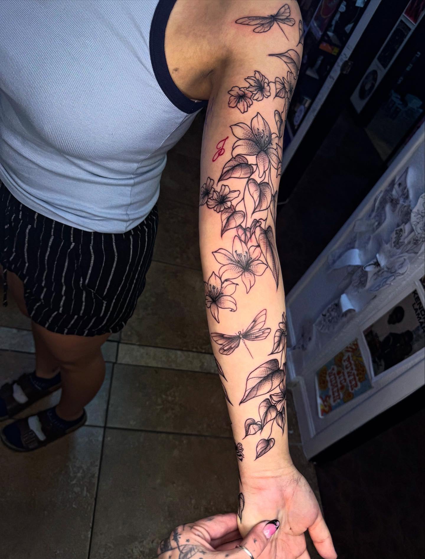 Lilies and dragonflies black and grey tattoo on the forearm by McKenna Hughes