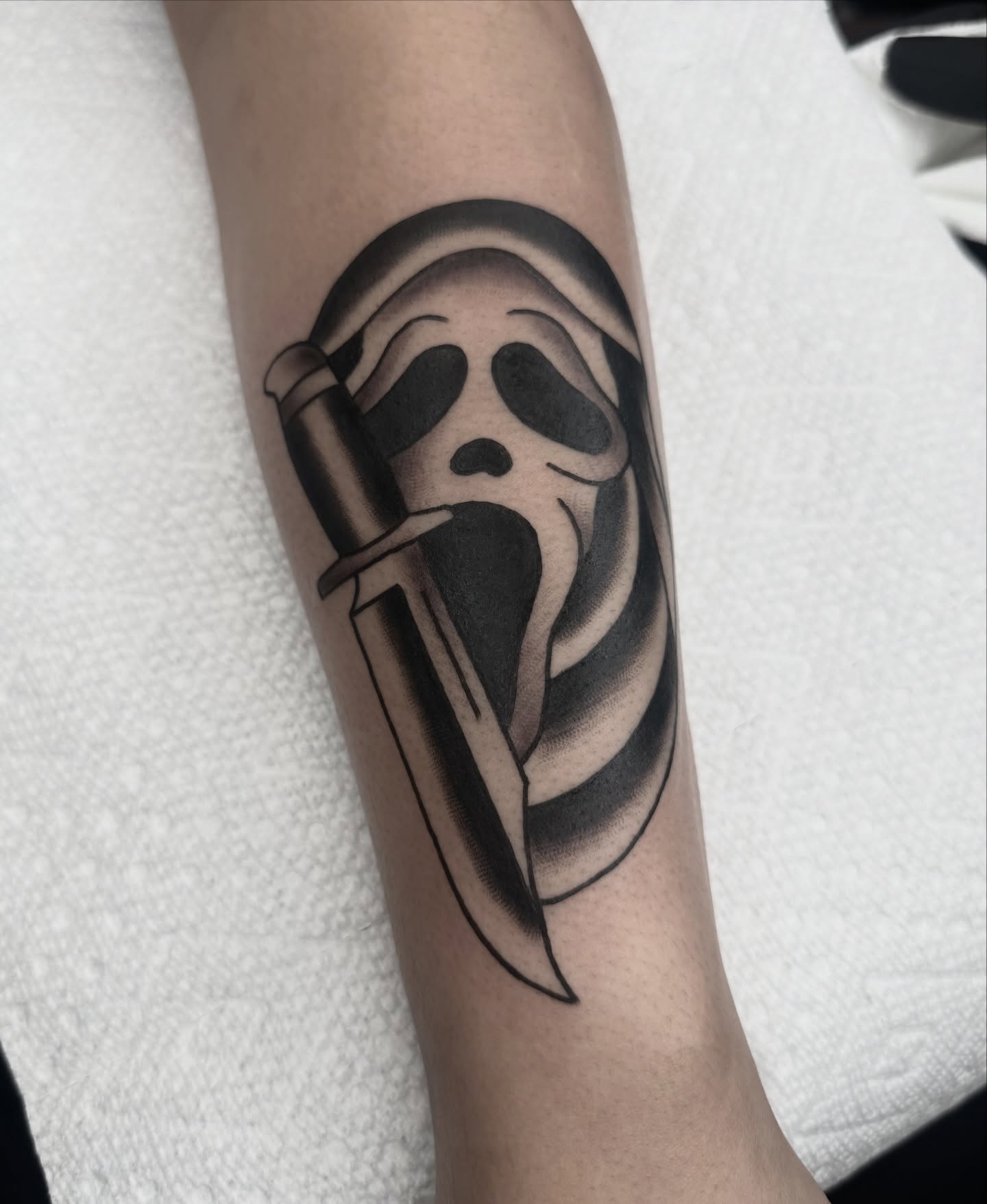 Ghost mask with knife black and grey tattoo on the forearm by Drew🕸️, Phoenix, Arizona