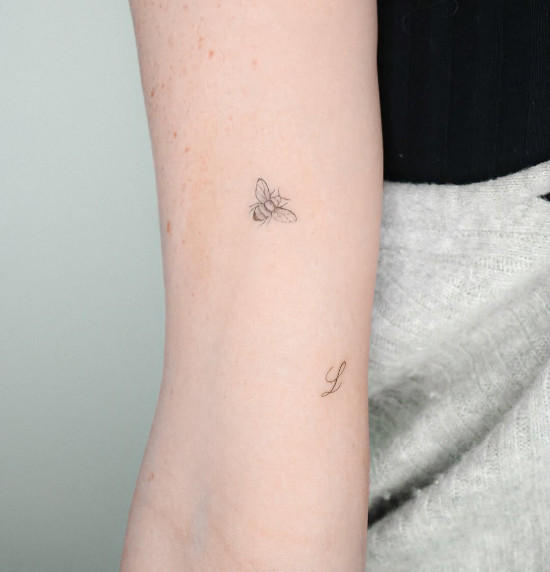 Bee and letter L minimalist tattoo on the forearm by Fine Line, New York, New York
