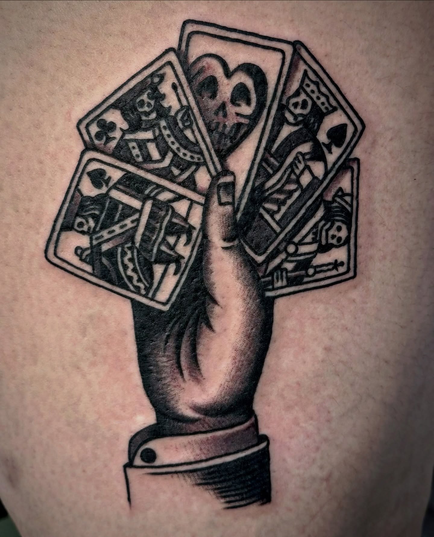 Hand holding playing cards realism tattoo on the upper arm by Pavel