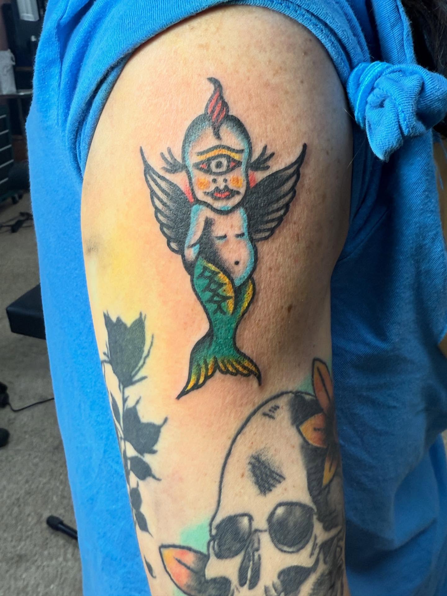 Mermaid with wings American traditional tattoo on the upper arm by Jesse Coldiron