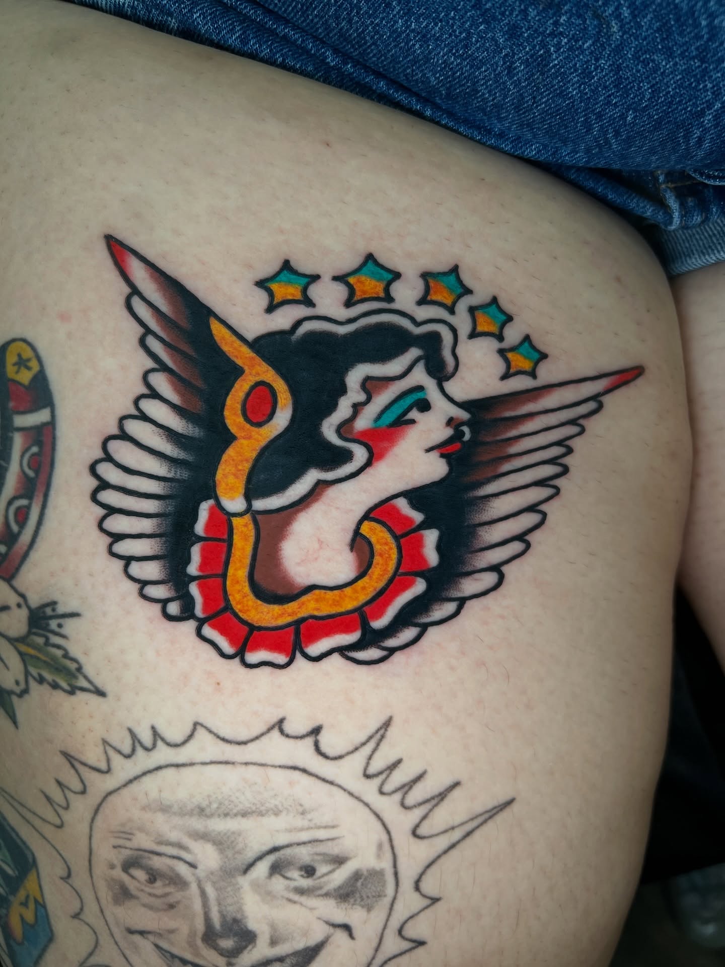 Angry face with wings American traditional tattoo on the thigh by 🍊Harvey Perez 🍊, Deerfield Beach, Florida