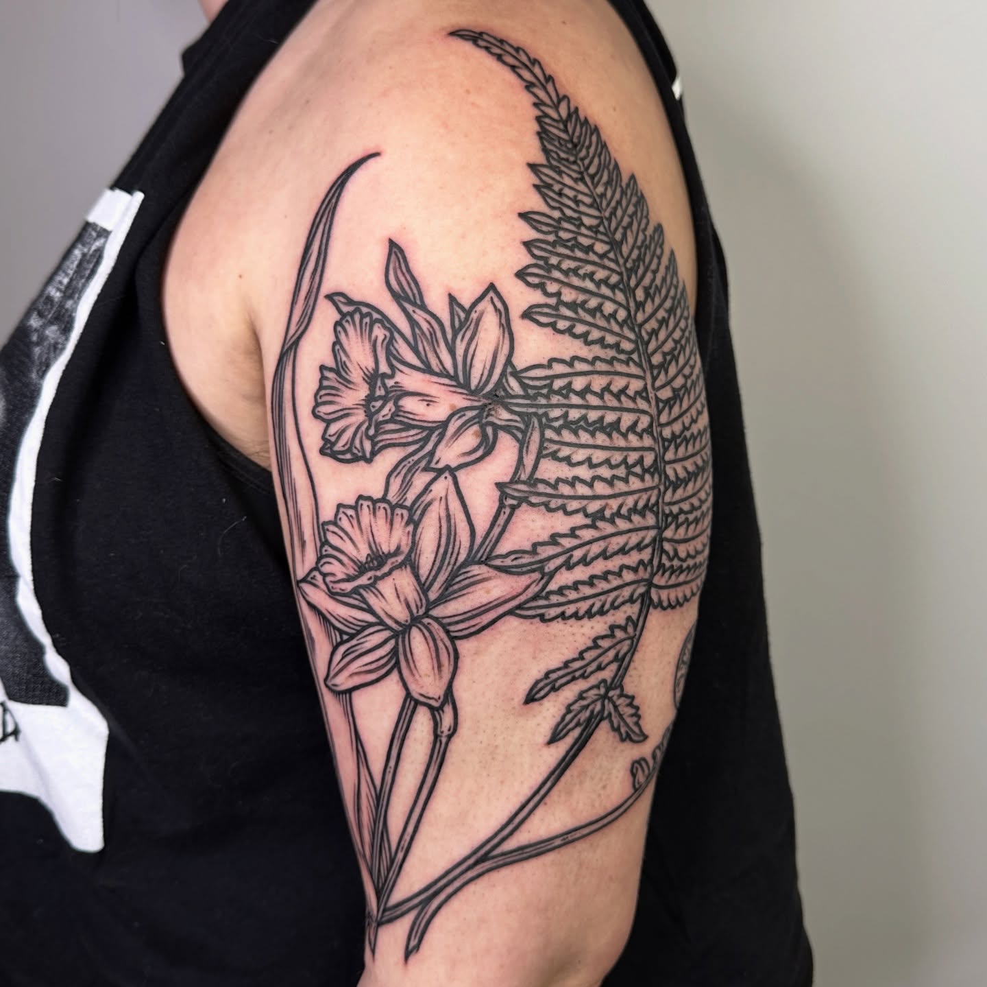 Daffodils and fern black and grey tattoo on the upper arm by rosalie