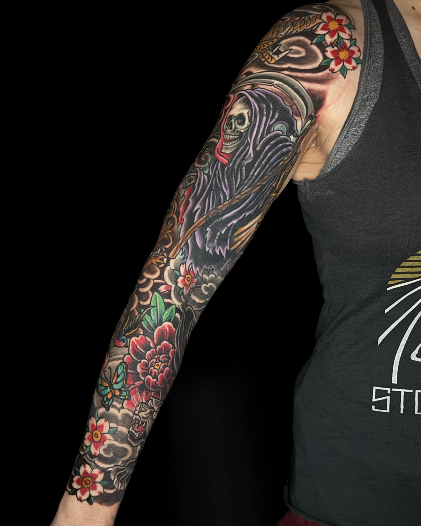 Skull and flowers American traditional tattoo on the upper arm by Chris Cockrill