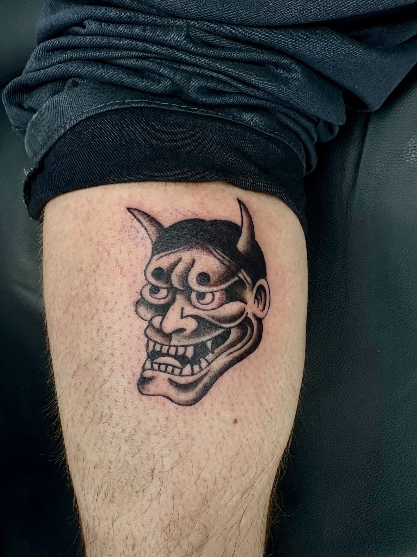 Demon mask black and grey tattoo on the thigh by Deacon Moser