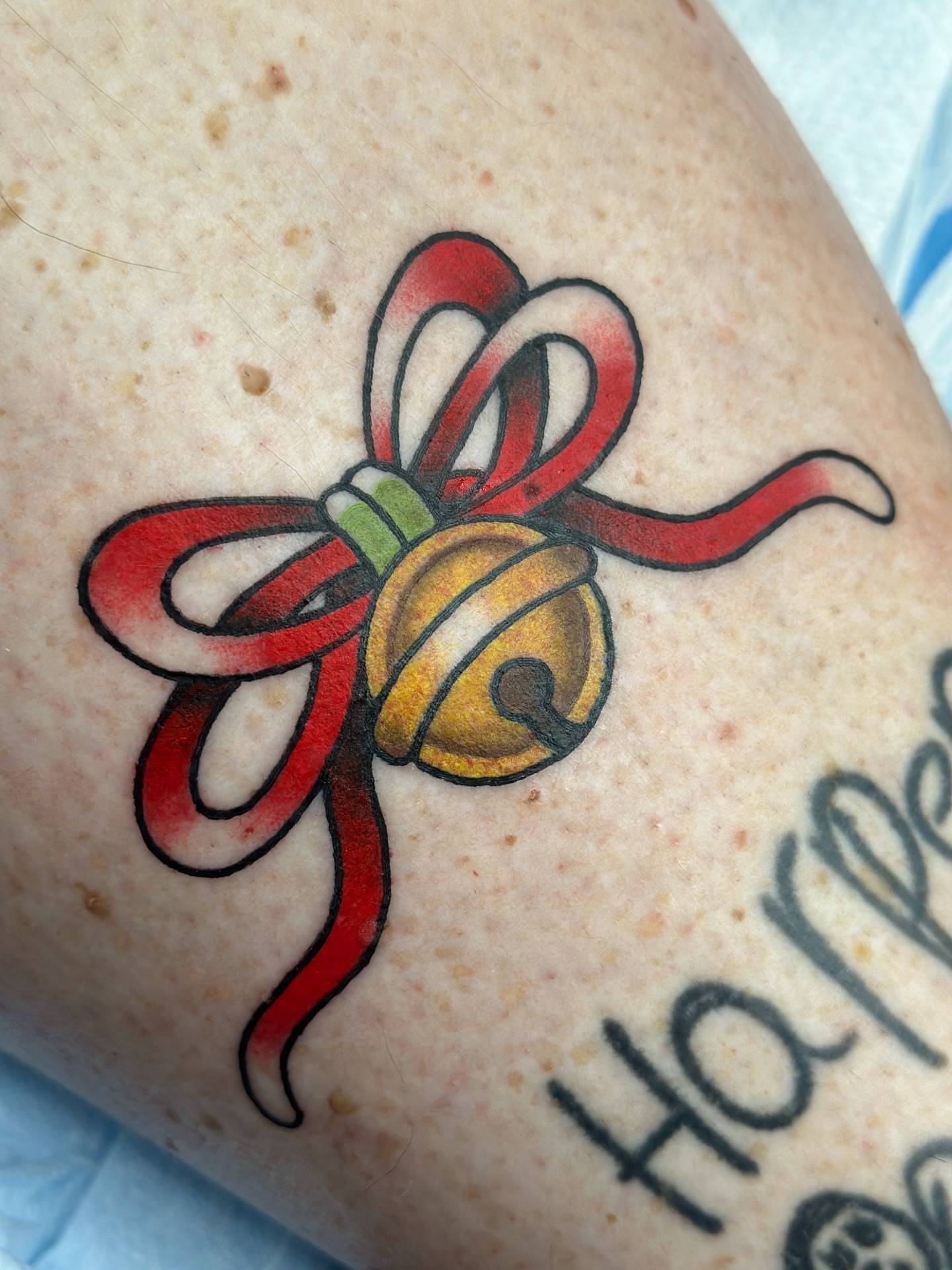Bell and ribbon American traditional tattoo on the forearm by Lucy Jay
