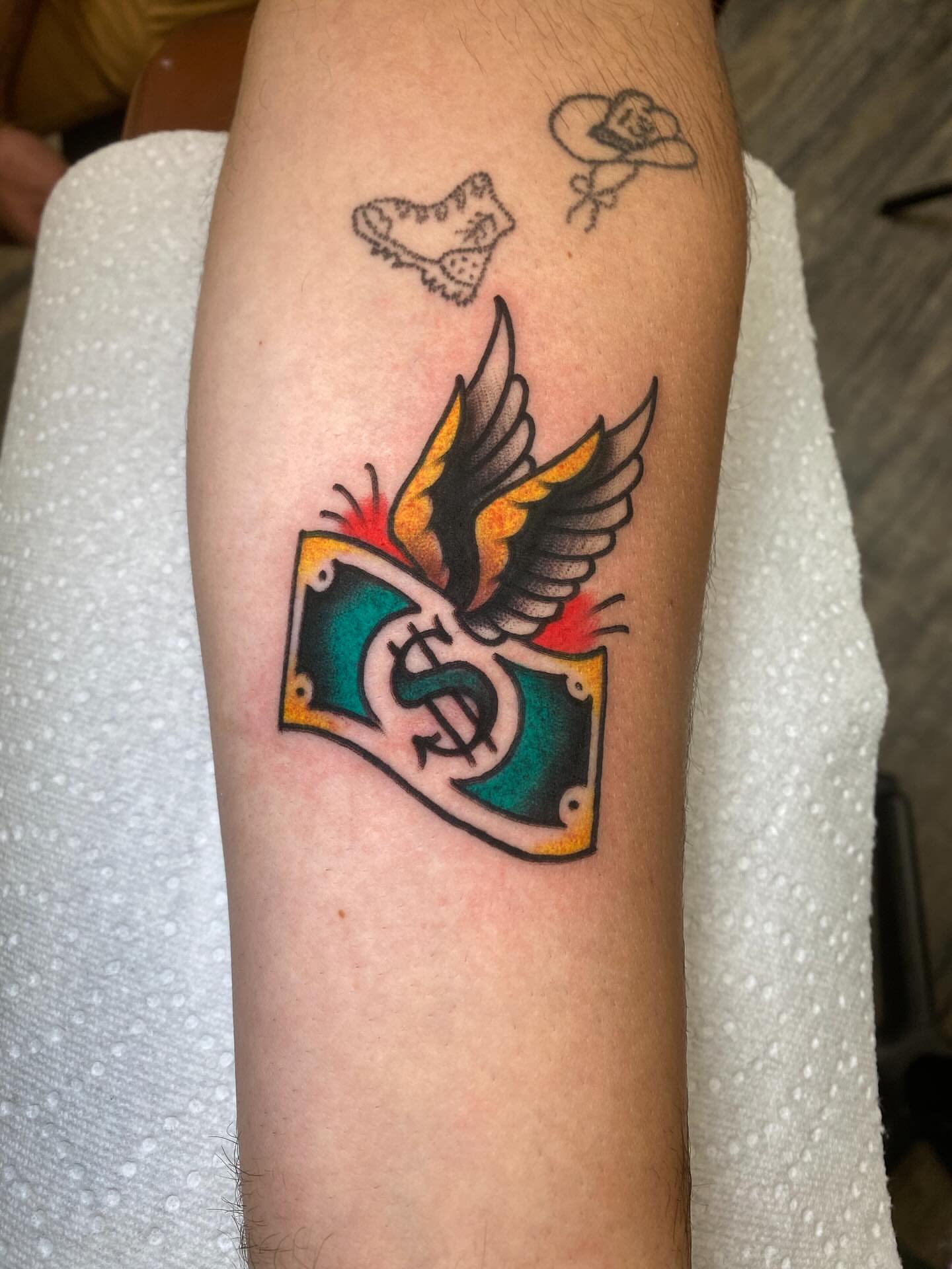 Money bill with wings American traditional tattoo on the forearm by Brandon Heredia, Vacaville, California