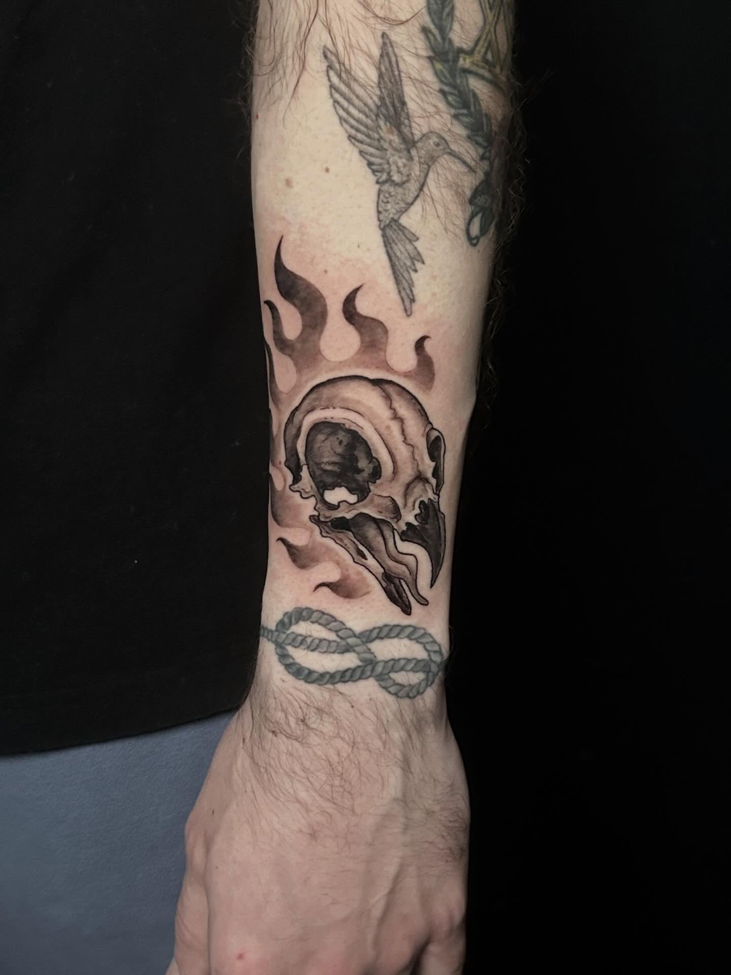 Skull with flame and bird realism tattoo on the forearm by Michigan Tattoo Artist - Emily Borneman