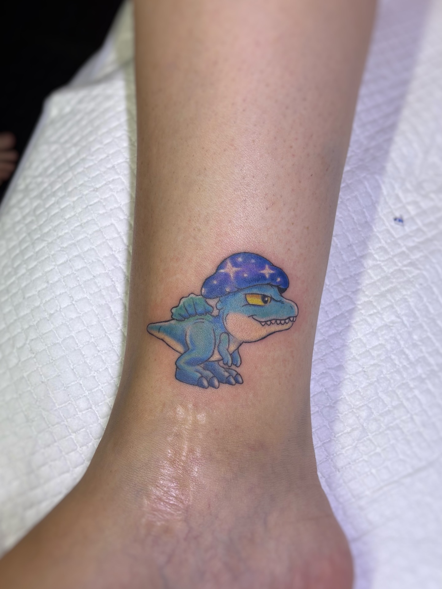 Dinosaur with hat new school tattoo on the forearm by Art by Aimee