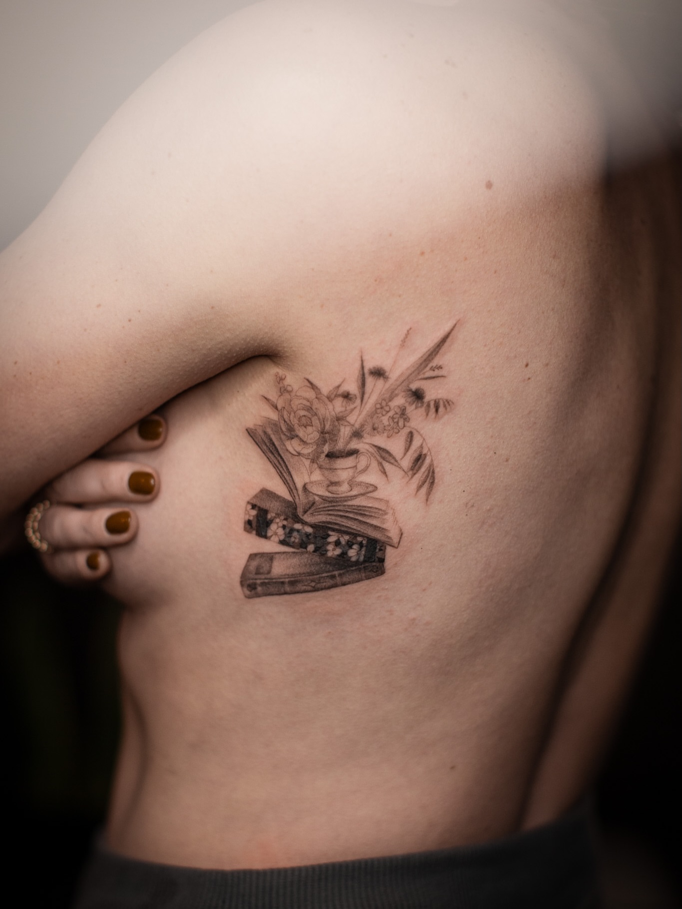 Book and flowers black and grey tattoo on the back by Aries Rising
