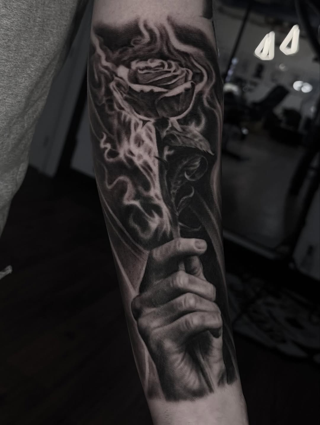 Hand holding a rose with smoke surrealism tattoo on the forearm by Jeremiah Warner
