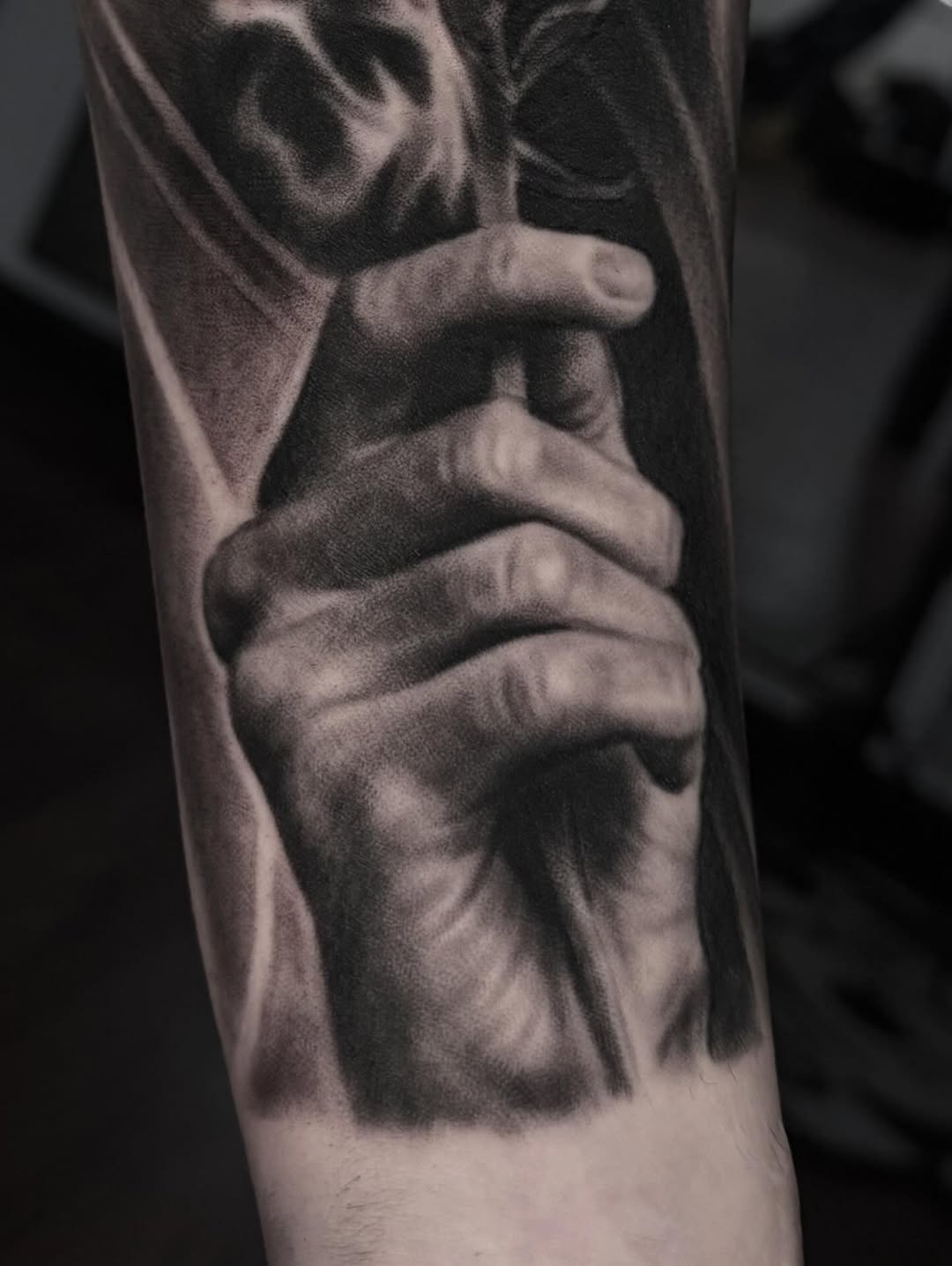 Hand holding a staff Chicano tattoo on the forearm by Jeremiah Warner