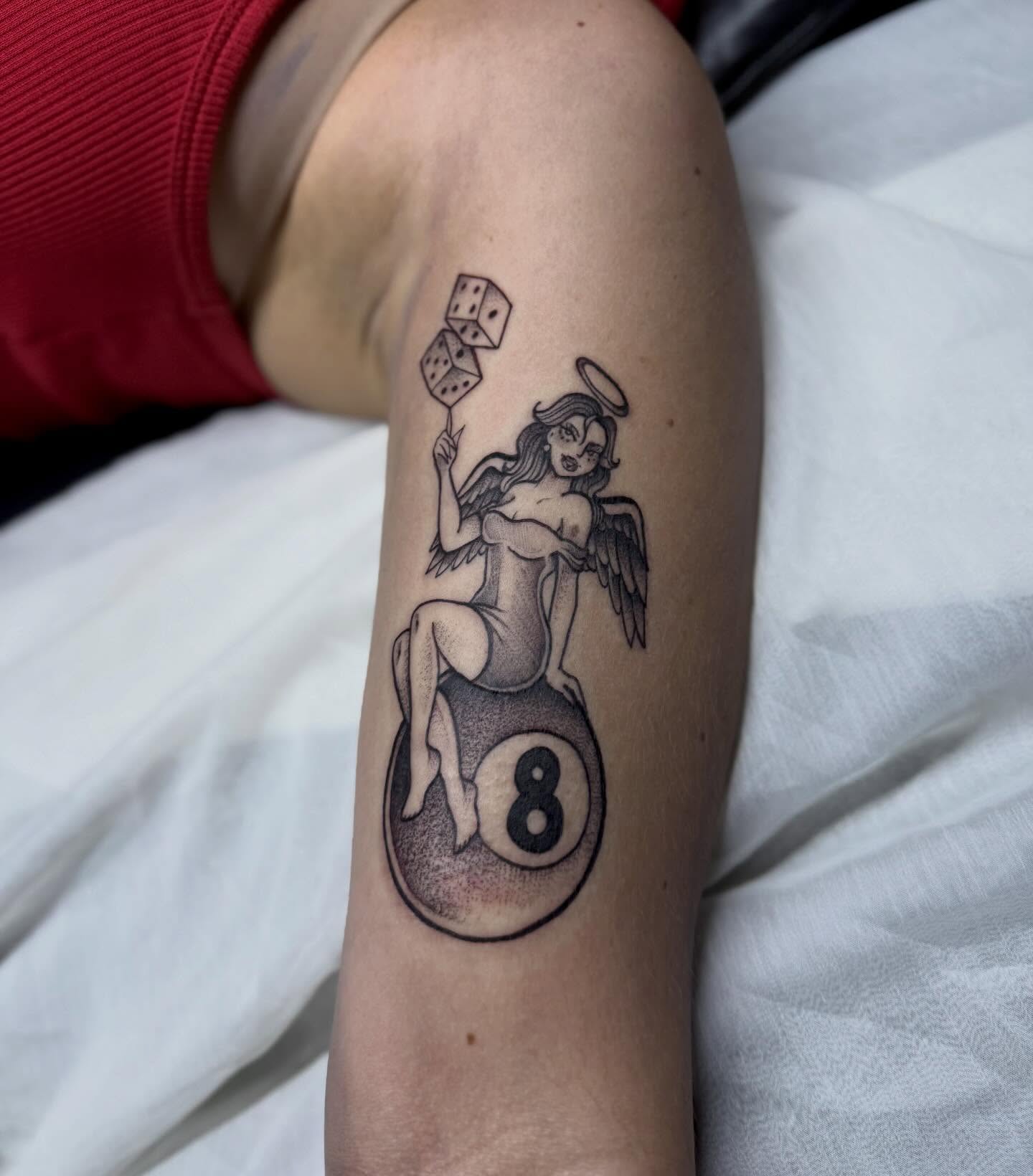 Angel with dice black and grey tattoo on the forearm by Sasha “Sashimi” Shabasov
