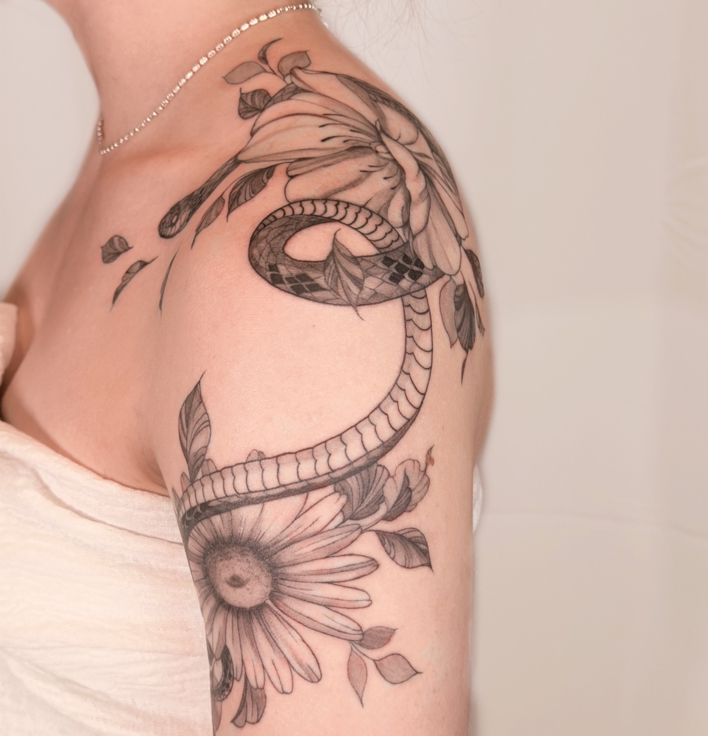 Snake and flower realism tattoo on the upper arm by Charlotte