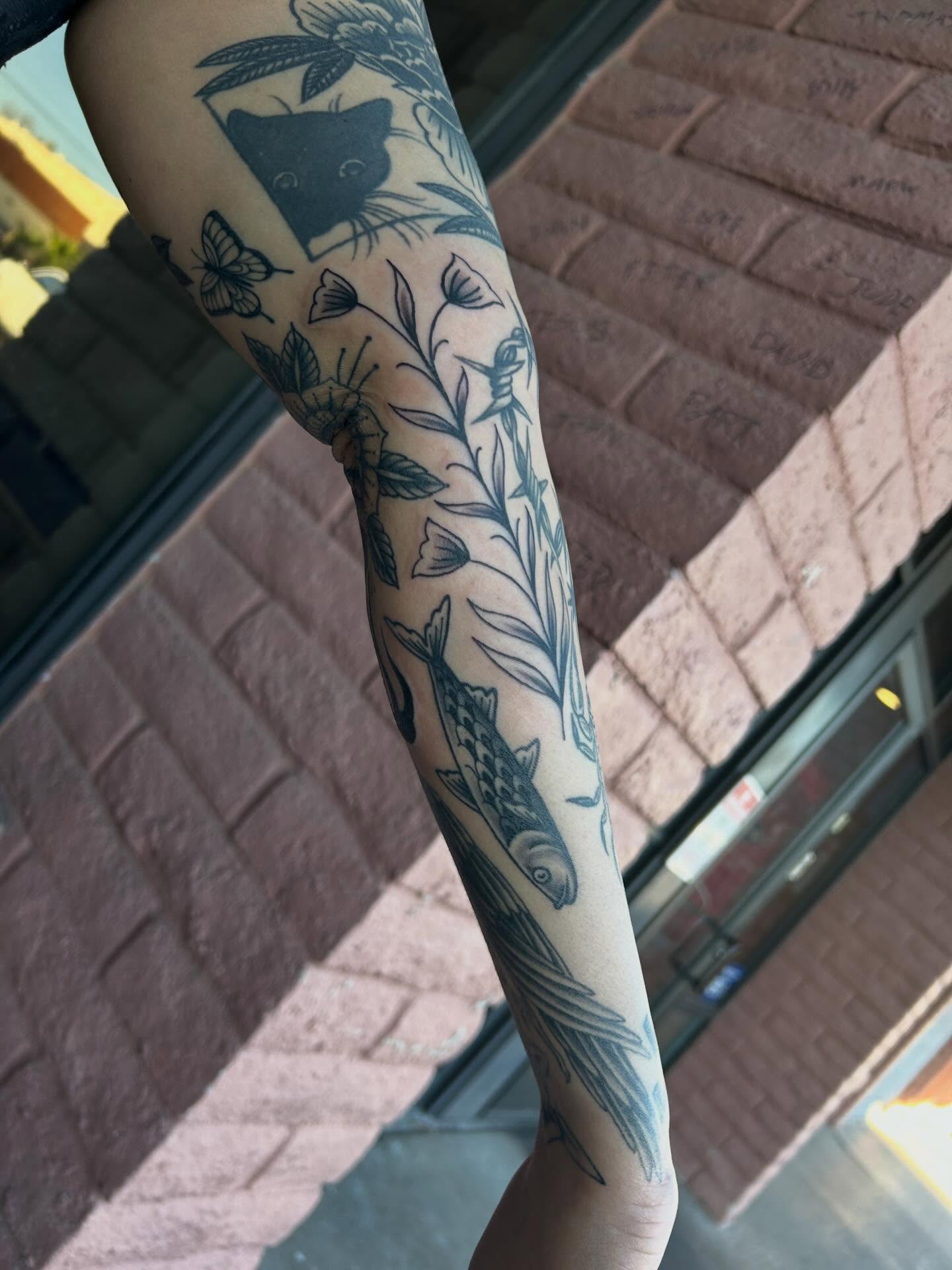 Fish and floral black and grey tattoo on the forearm by Janelle McCarthy