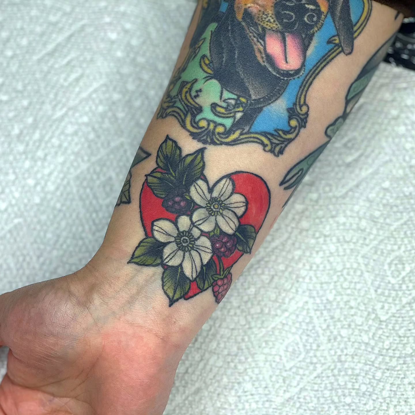 Dog and heart with flowers American traditional tattoo on the forearm by Amanda Hinrichs